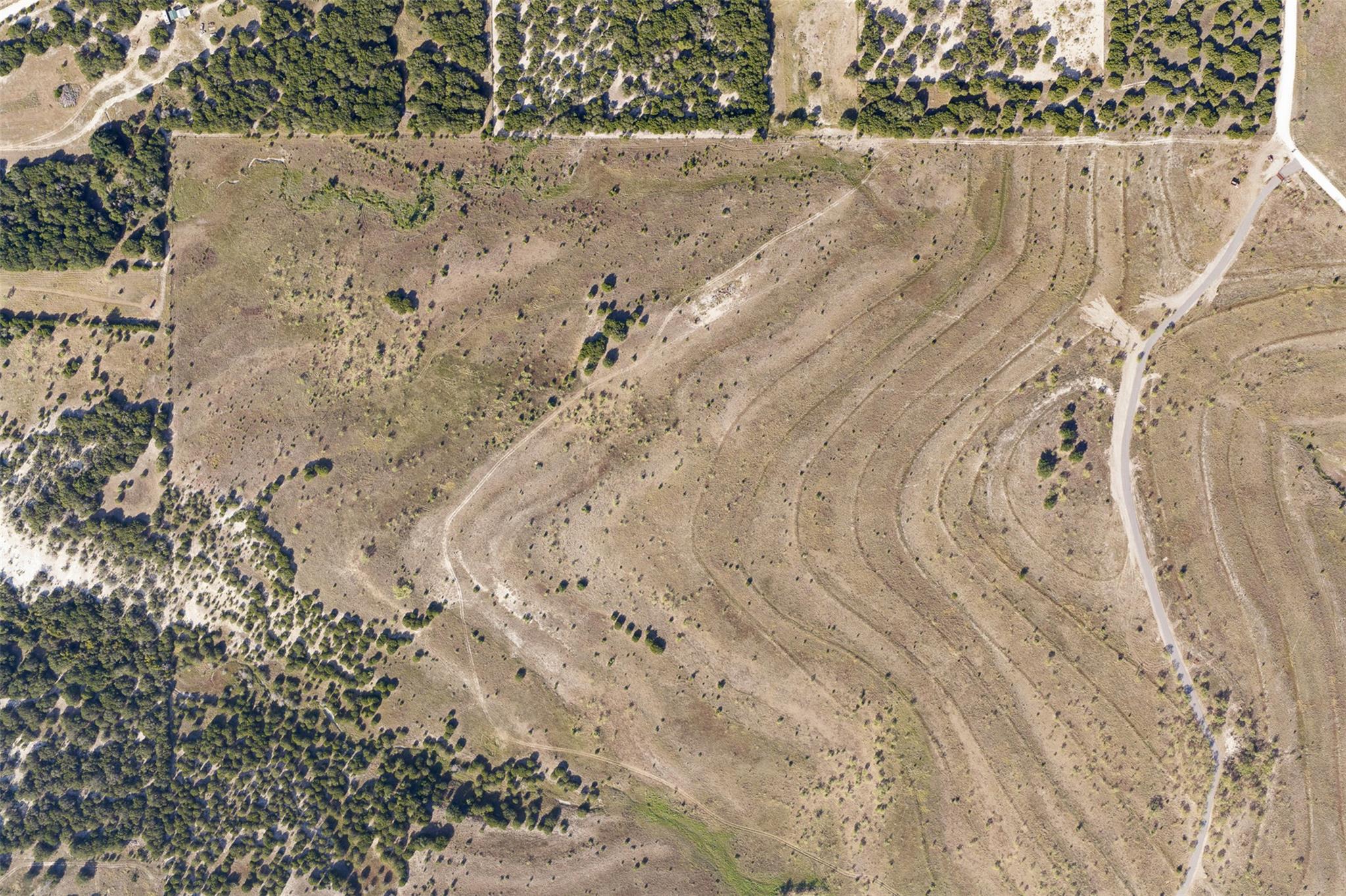 Aerial view of open, scrub-covered acreage bordered by trees, with tracks and a paved road.