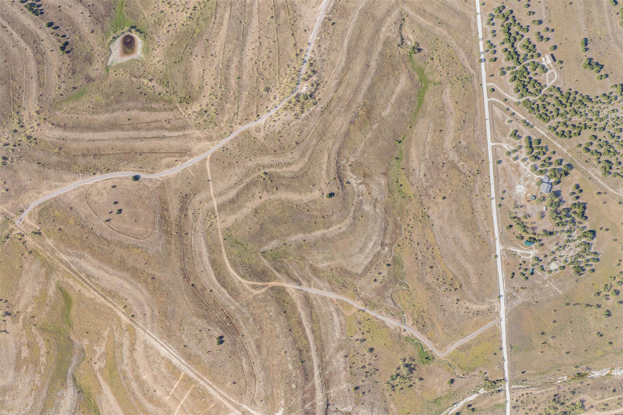 Aerial view of dry, rolling land with winding tracks, sparse trees, and a paved road.