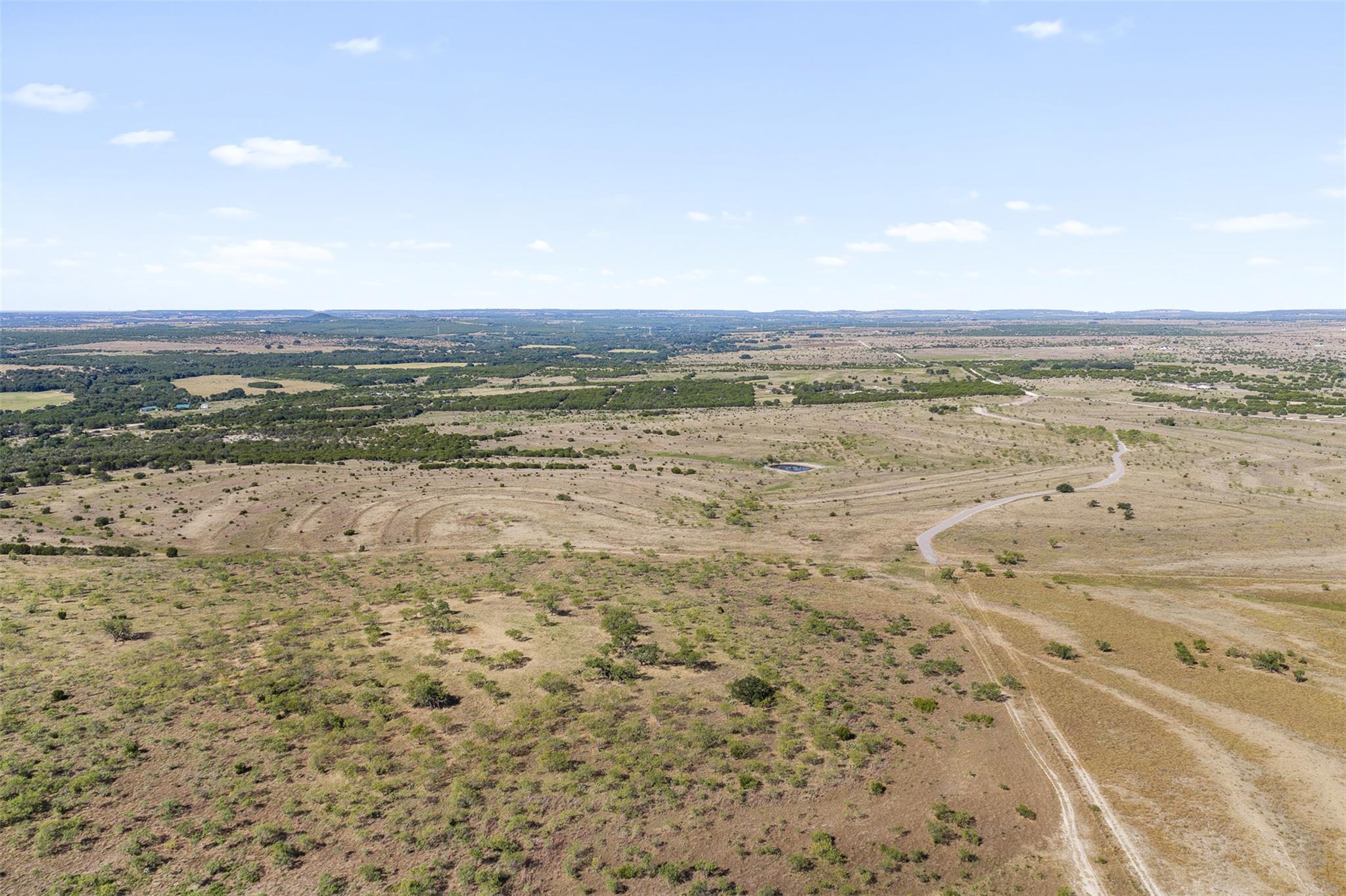 Aerial view of dry, scrub-covered acreage with a winding road and small pond.