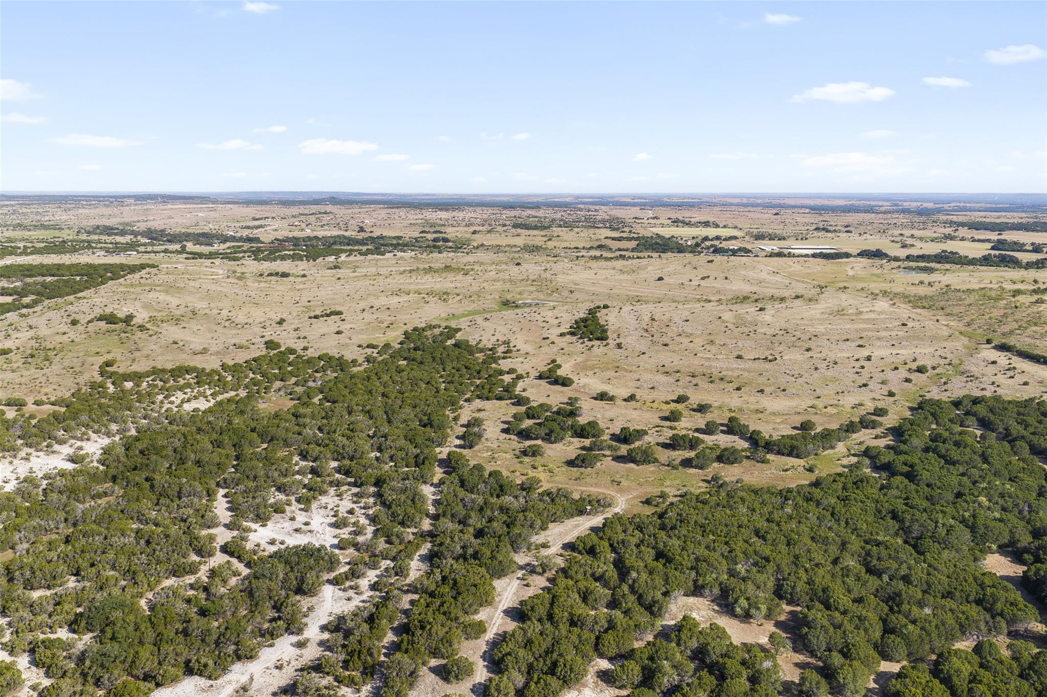 Aerial view of rural brushland with open grassland and winding dirt tracks.
