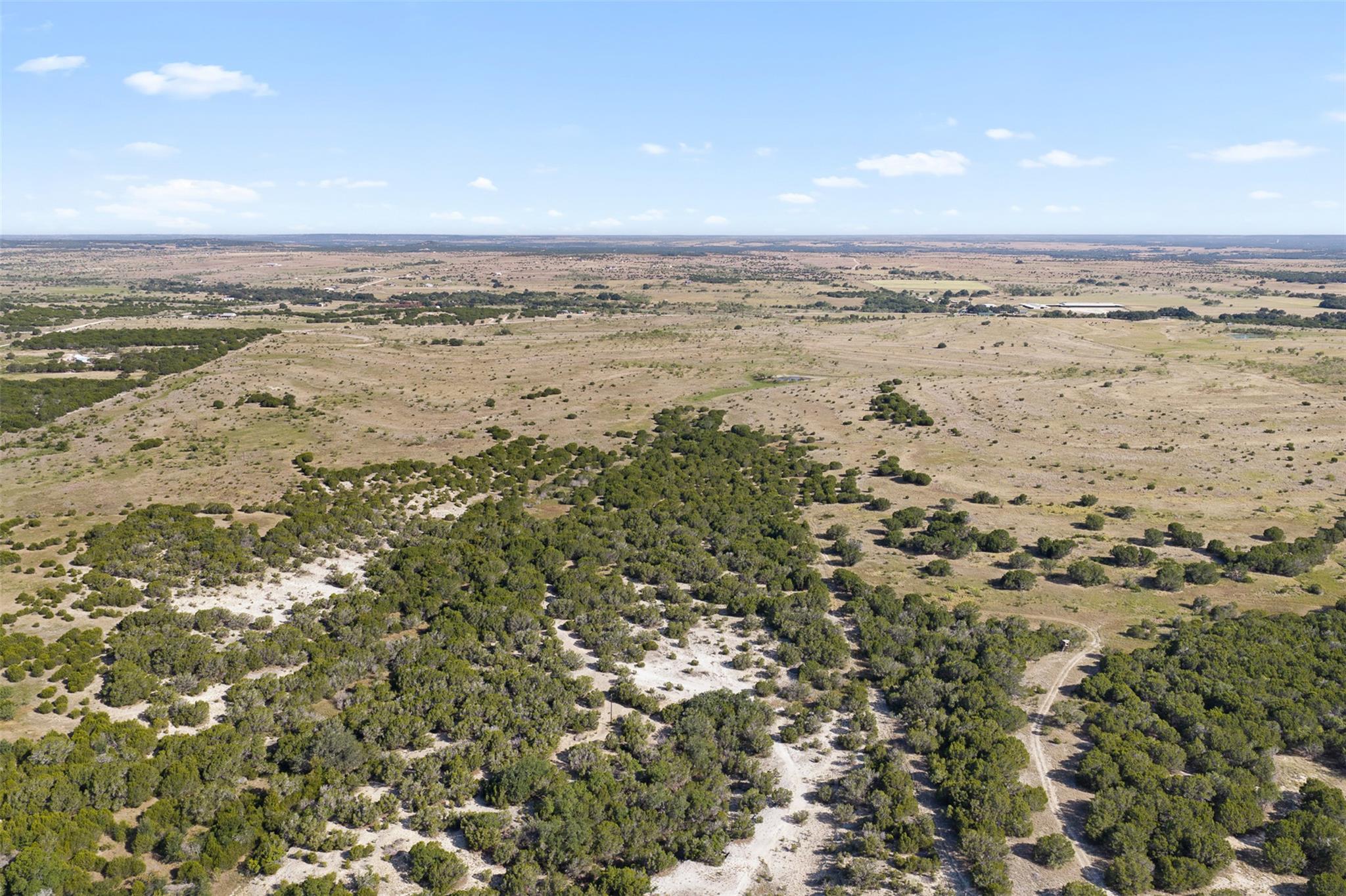 Aerial view of vacant rural land with scrub trees, dry grassland, and winding dirt tracks.