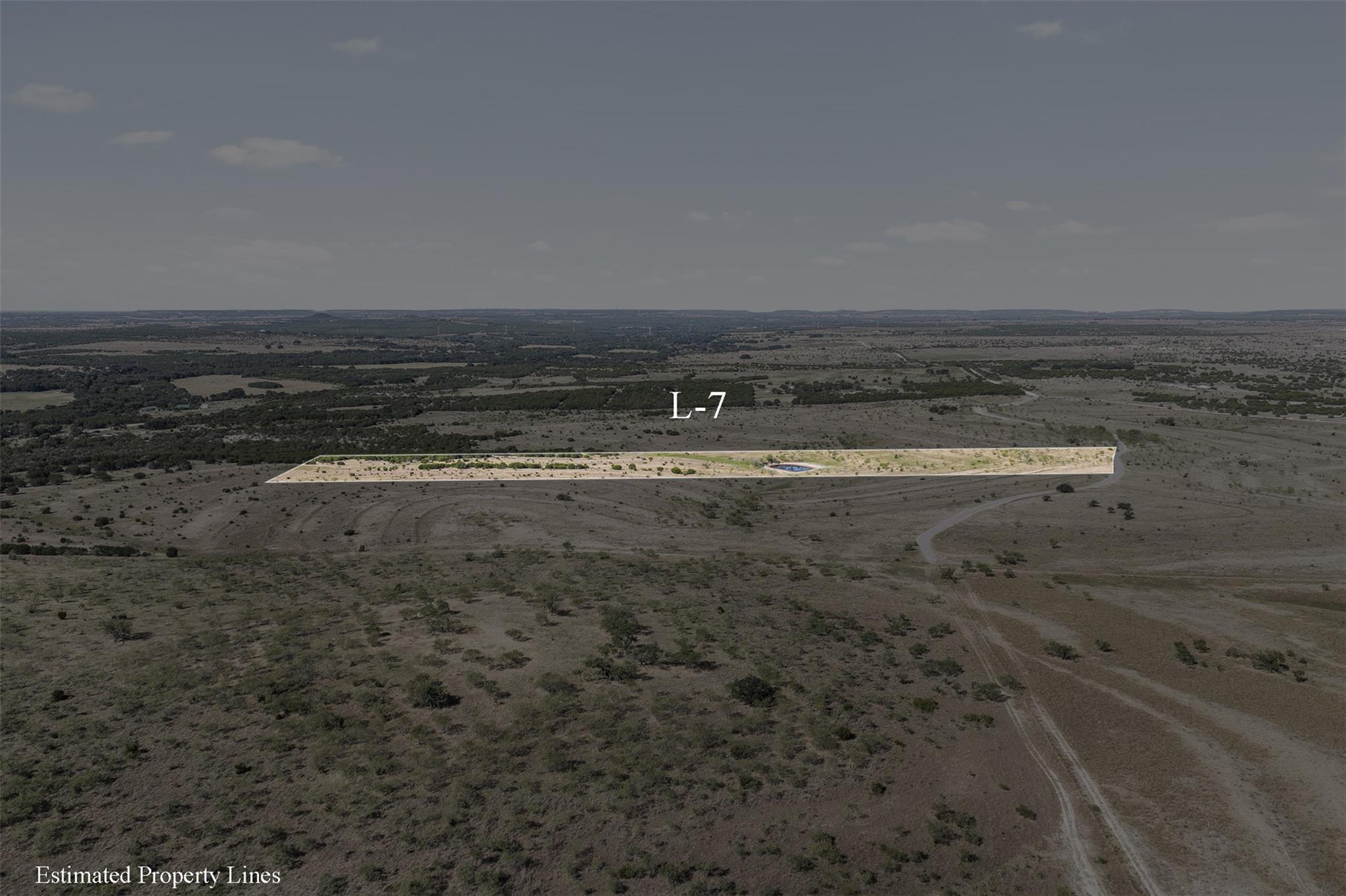 Aerial view of the long L-7 parcel outlined across dry countryside, with a small pond and nearby dirt road.