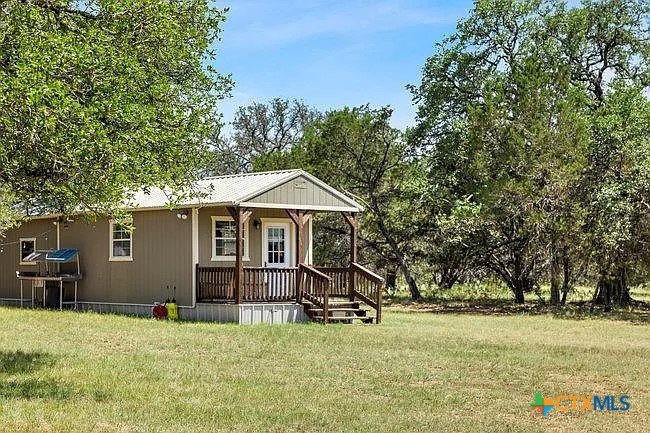 Single-story home with a covered wooden porch in a grassy, tree-lined clearing.