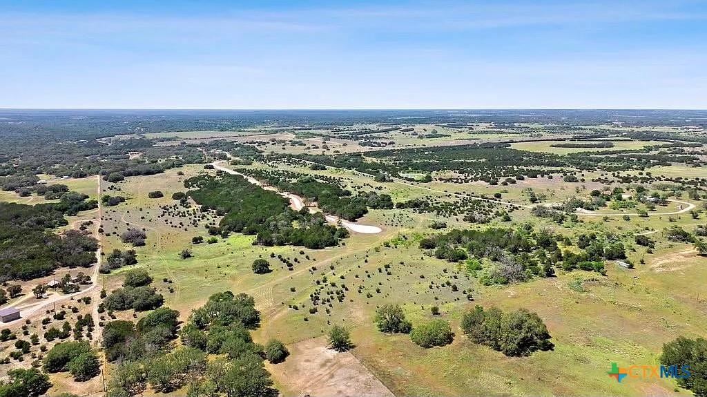 Aerial view of open ranch land with scattered trees, fields, and winding dirt roads.
