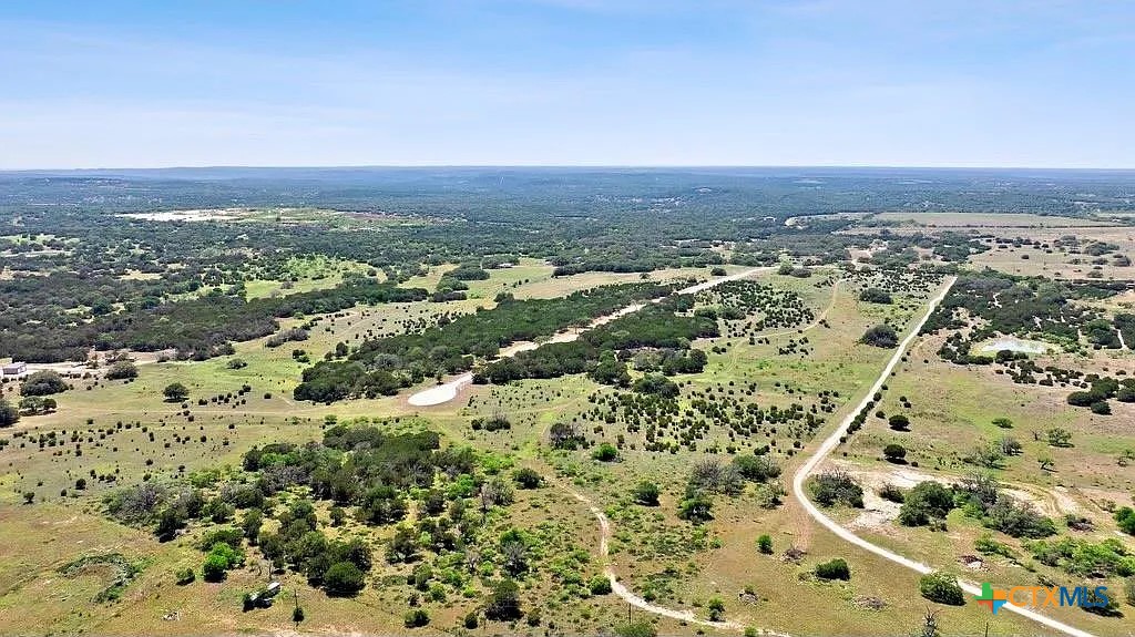 Aerial view of open rural acreage with scattered trees, wooded patches, and a winding dirt road.
