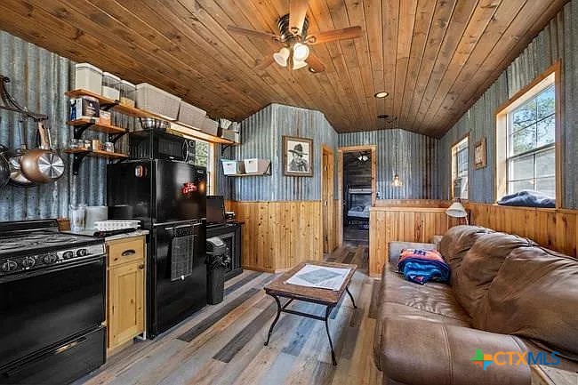 Kitchen and living area with black appliances, a leather sofa, and wood-paneled walls and ceiling.