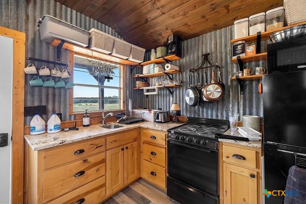 Rustic kitchen with wood cabinets, corrugated metal walls, and a window overlooking the countryside.