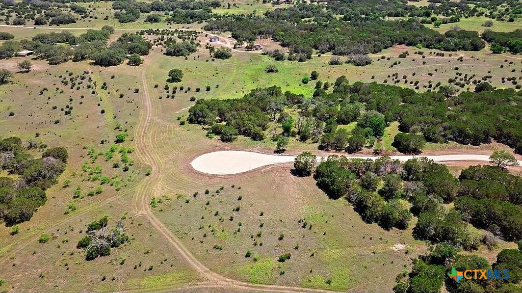 Aerial view of rural acreage with scattered trees and a pale driveway connecting to a road.