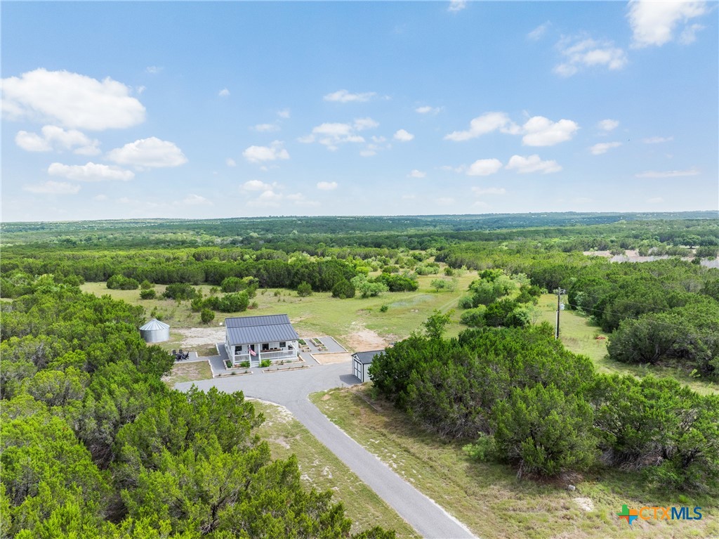 Aerial view of a rural property with a small metal-roofed building and gravel drive amid green wooded land.
