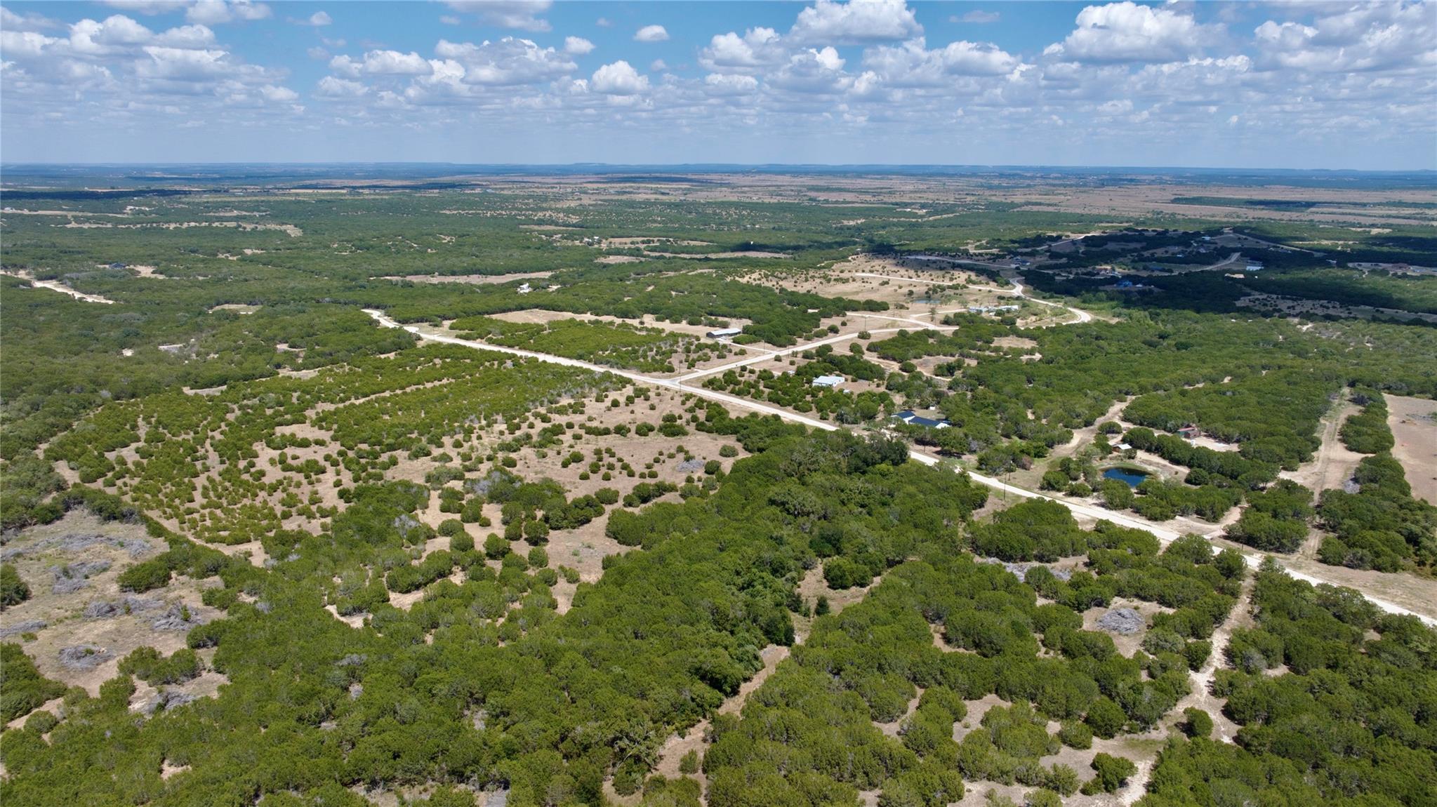 Aerial view of brush-covered rural land with winding dirt roads and a small pond.