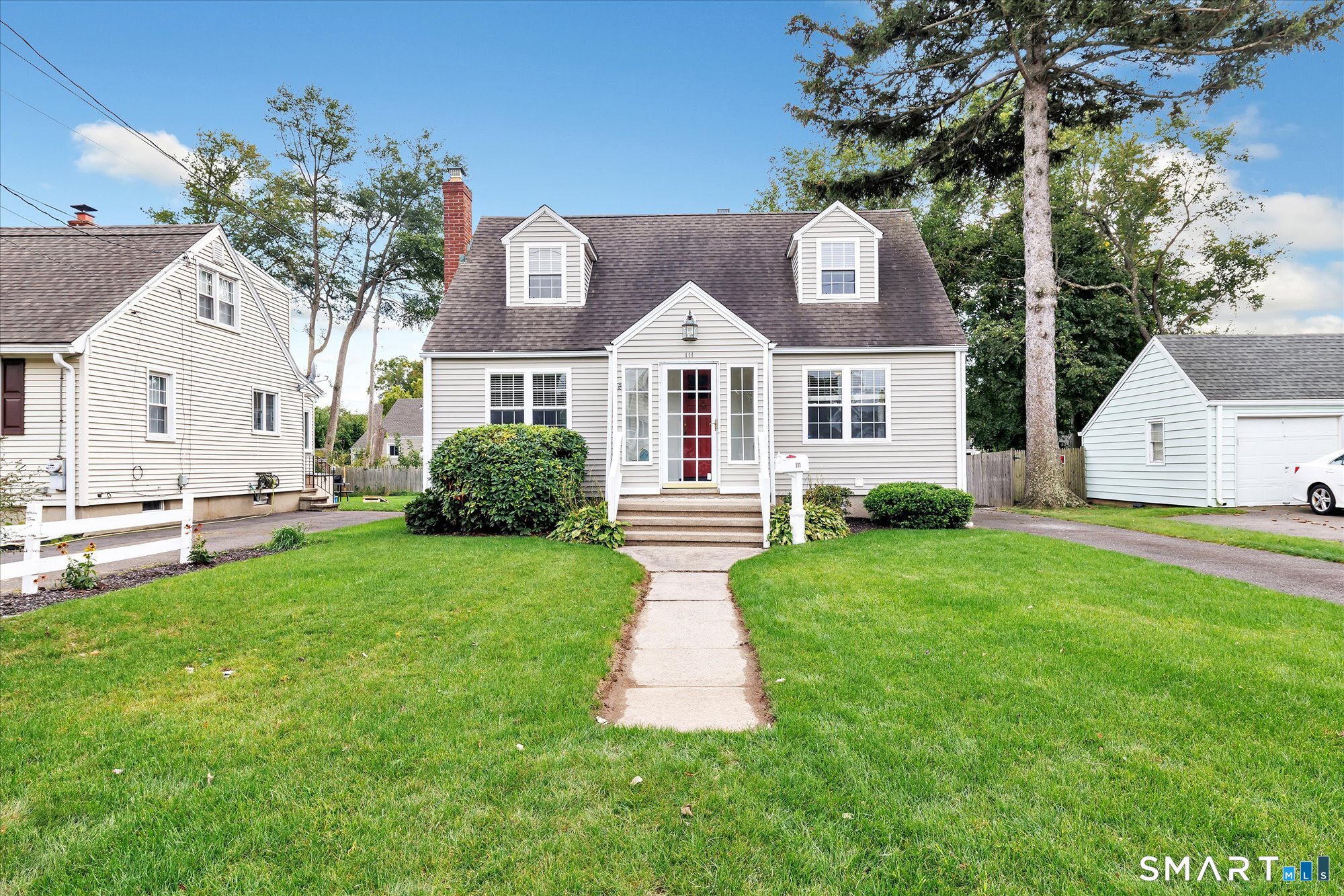 Cape-style house with two dormers, a red front door, and a broad green front lawn.