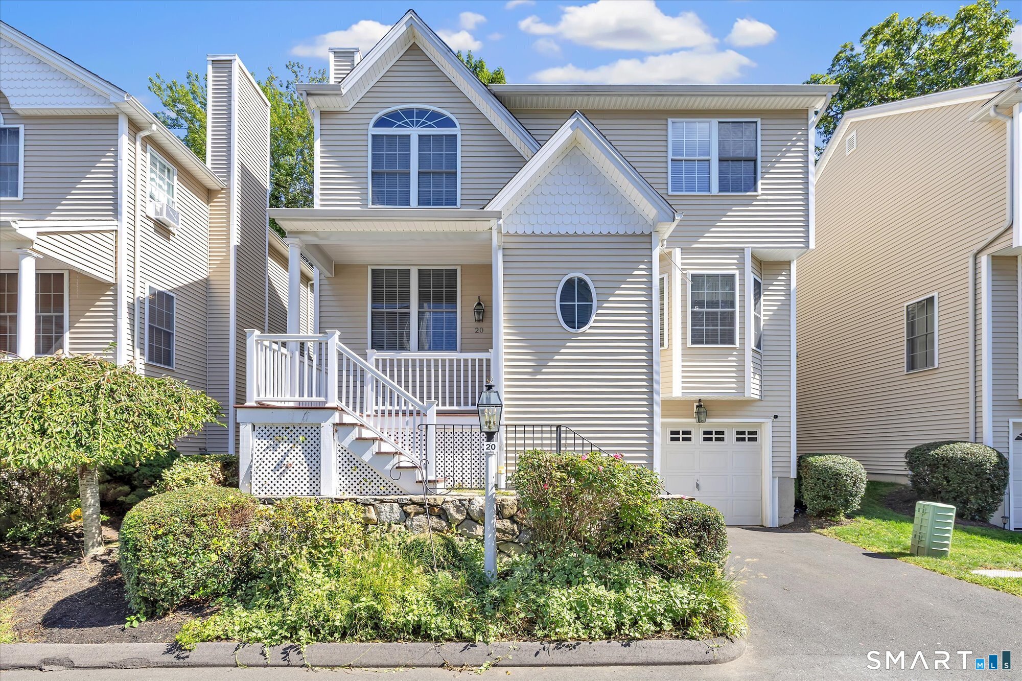 Gray townhouse with a white-railed porch, attached garage, and distinctive arched and oval windows.
