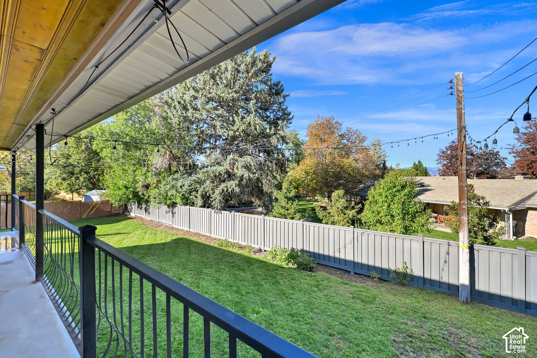 Covered porch overlooking a fenced lawn with mature trees and overhead string lights.