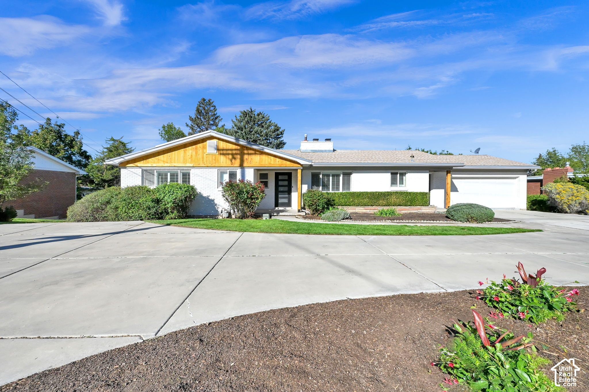 Single-story white-brick home with a wood-accented gable, attached garage, and wide concrete driveway.