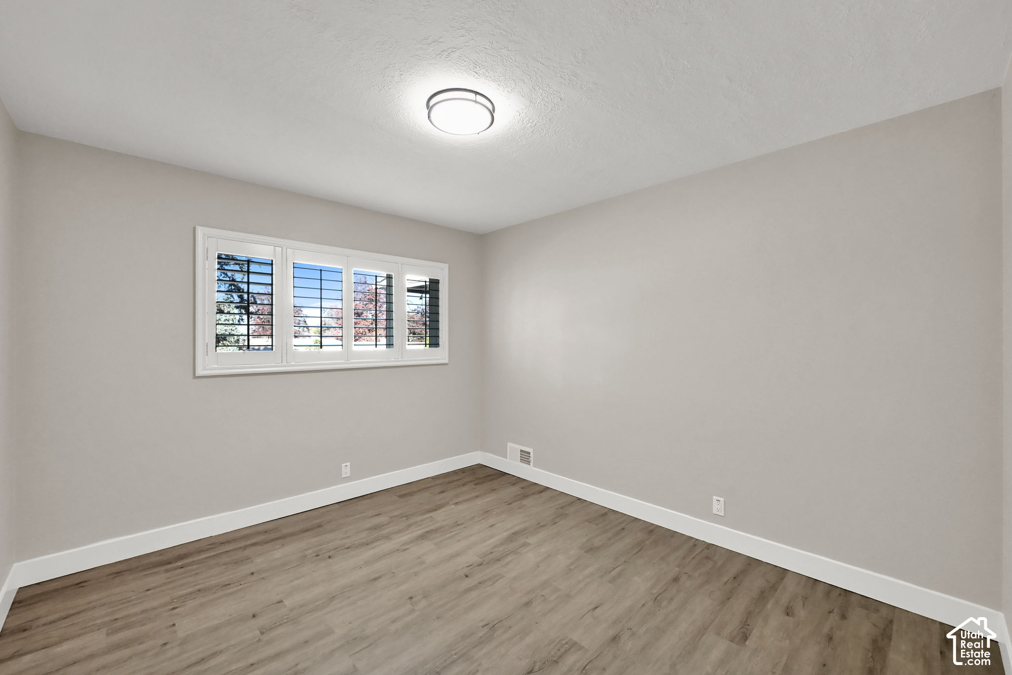 Empty room with wood-look flooring and a wide window fitted with plantation shutters.