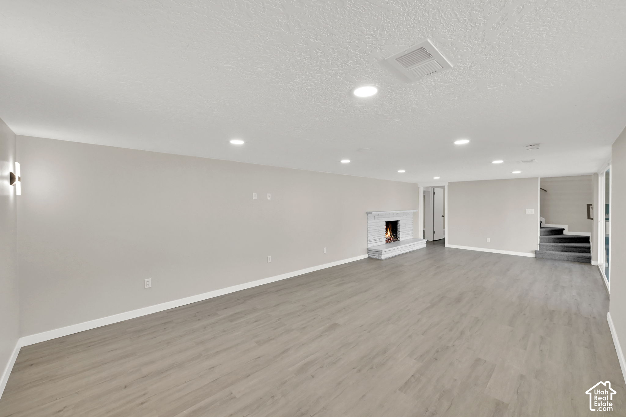 Vacant living room with gray plank flooring, a white brick fireplace, and carpeted steps.