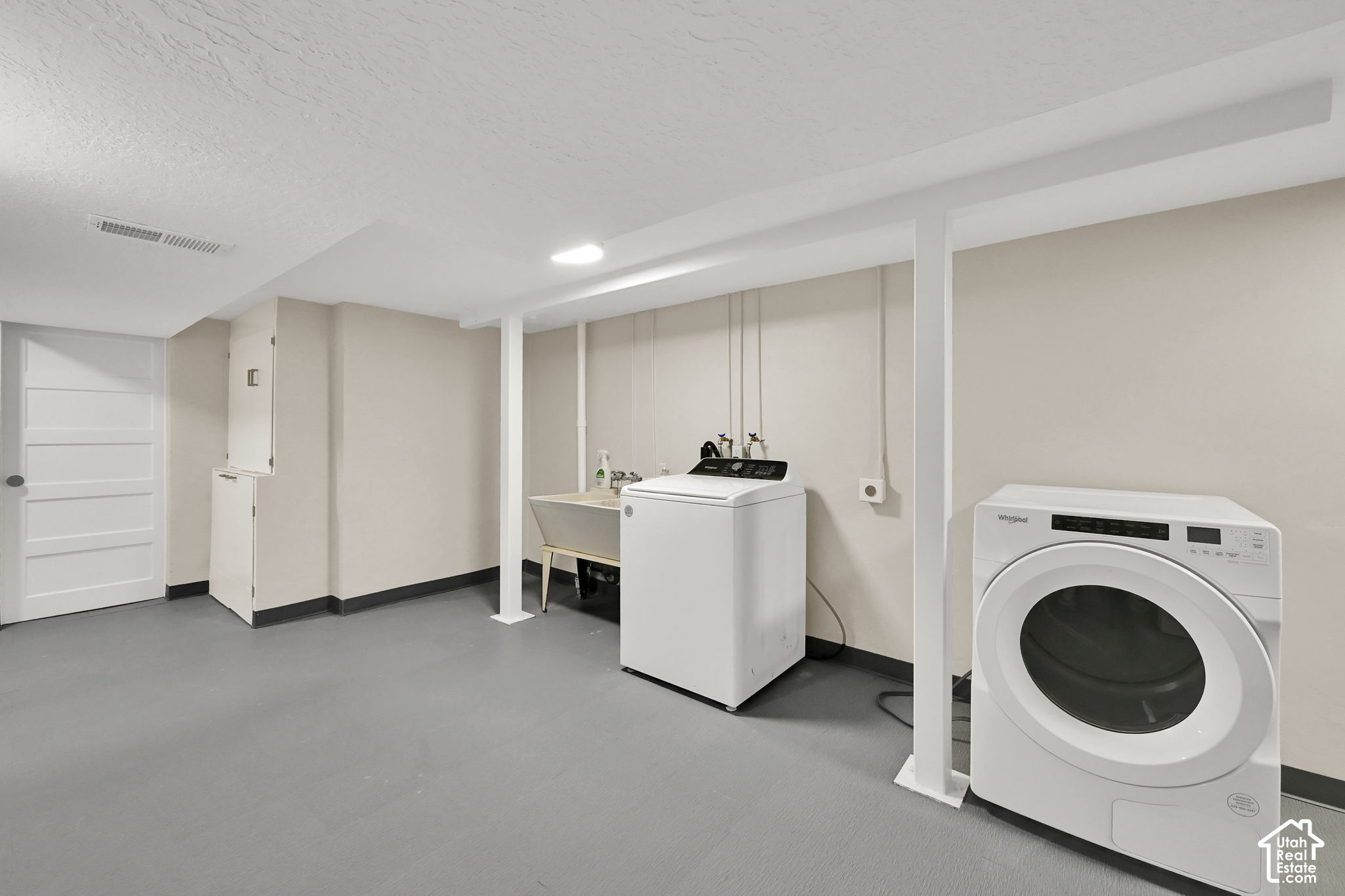 Basement laundry room with a top-loading washer, front-loading dryer, and utility sink.