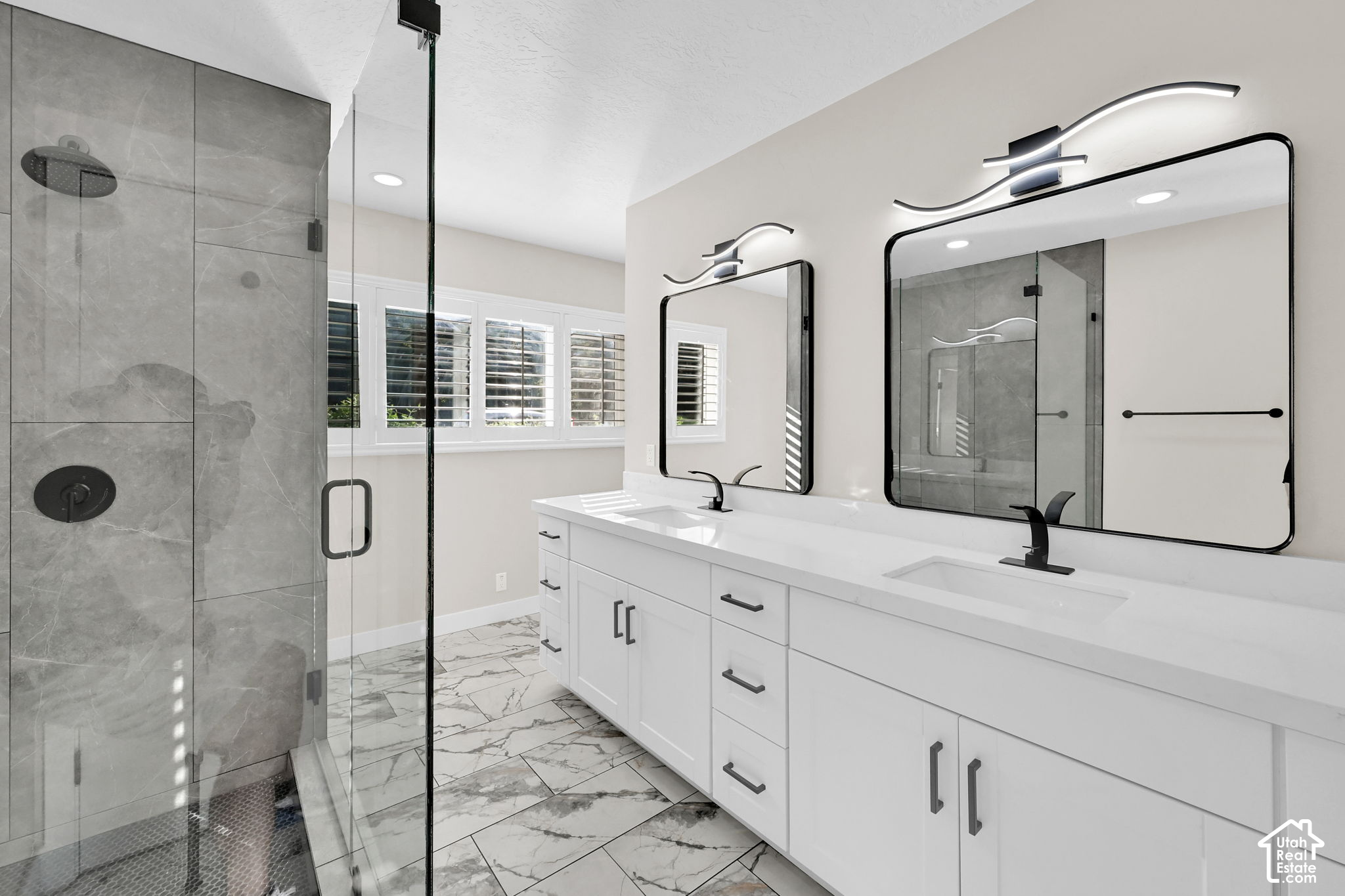 Bathroom with a double vanity, black fixtures, and a glass-enclosed gray-tile shower.