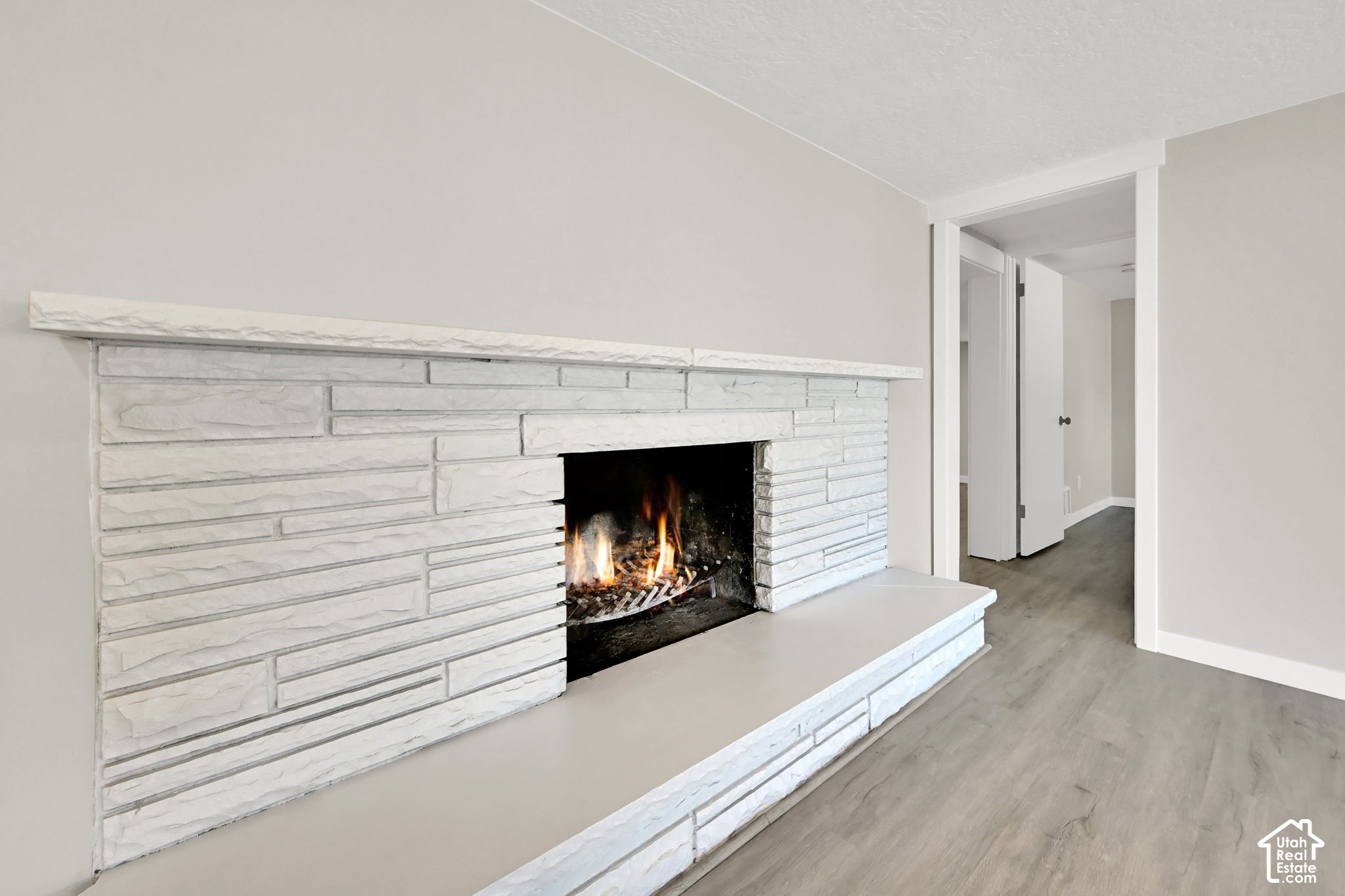 White stone fireplace with a lit fire and long hearth in an unfurnished room.