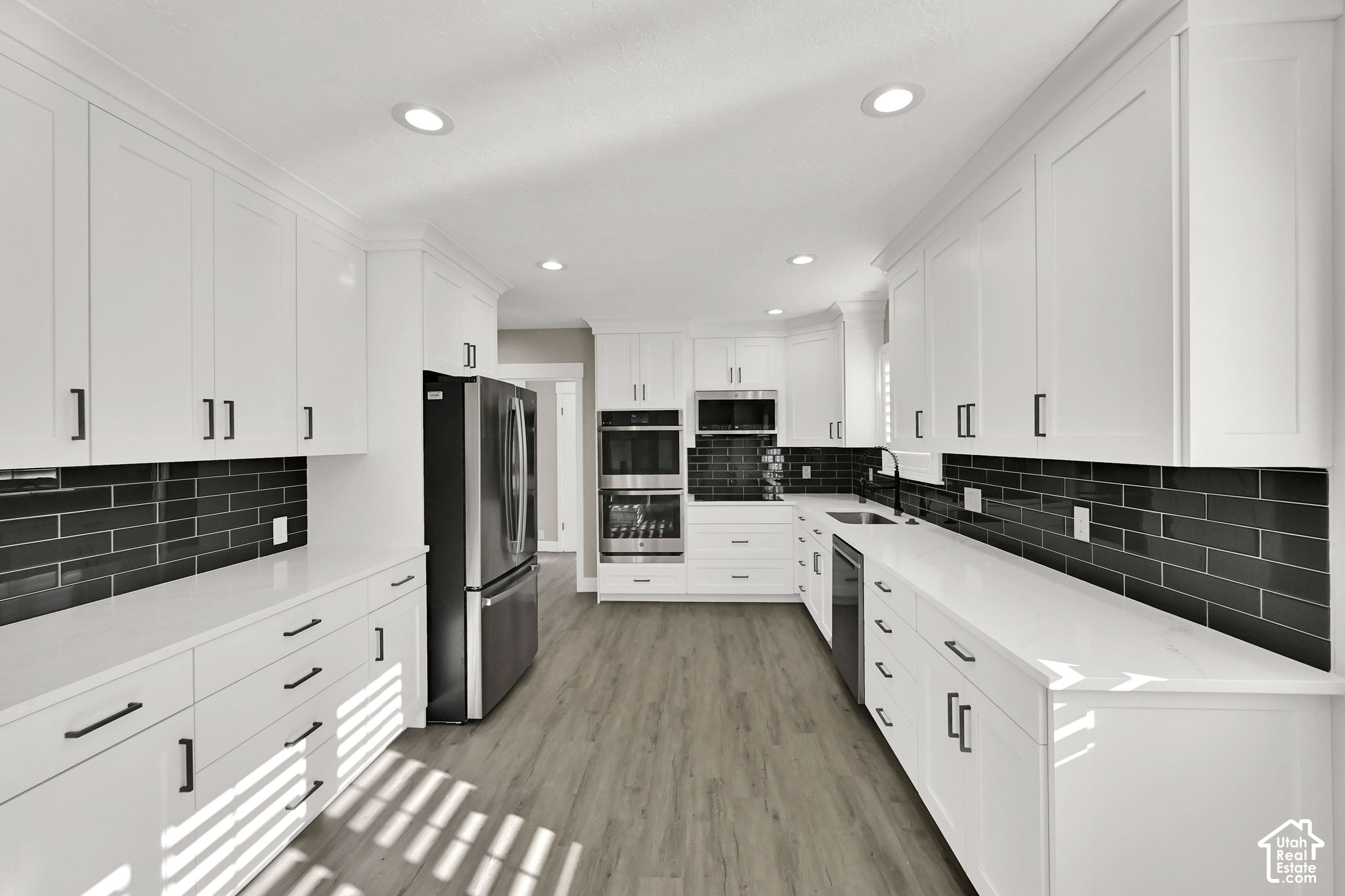 Renovated kitchen with white cabinets, black tile backsplash, and stainless steel appliances.