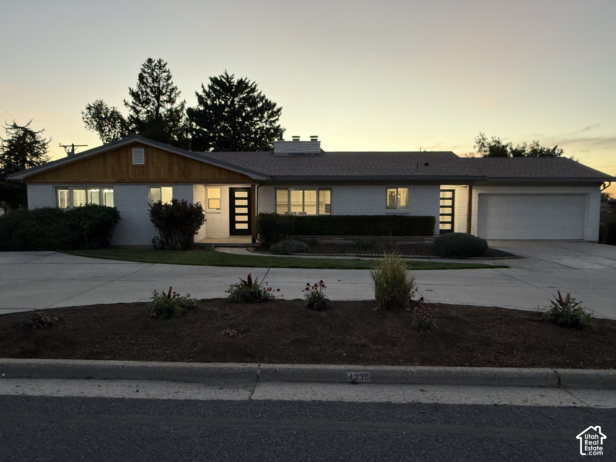 Single-story ranch home with white siding, a wood-accented gable, and an attached garage at dusk.