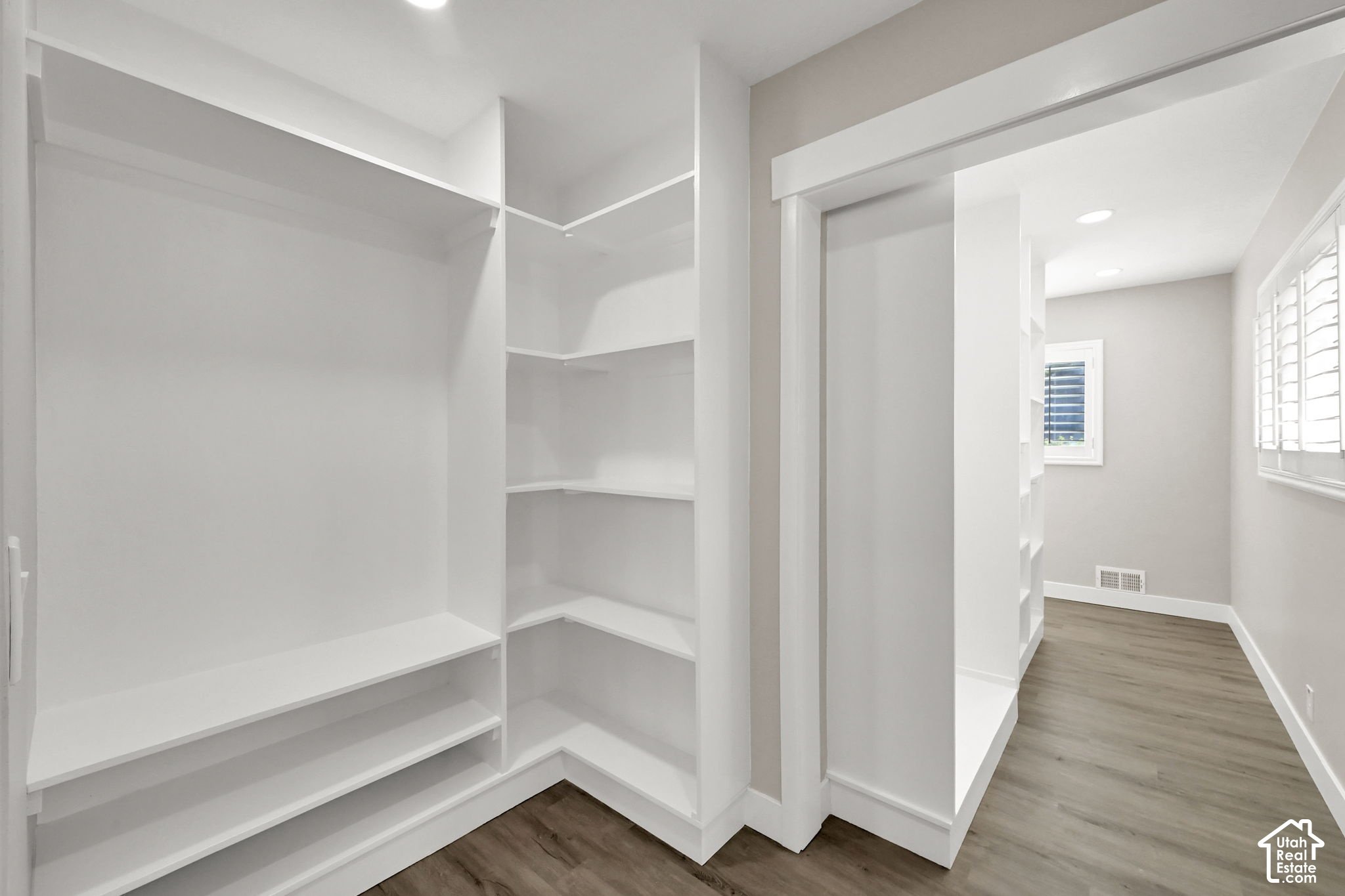 Walk-in closet with white built-in shelves opening to a dressing area with shuttered windows.