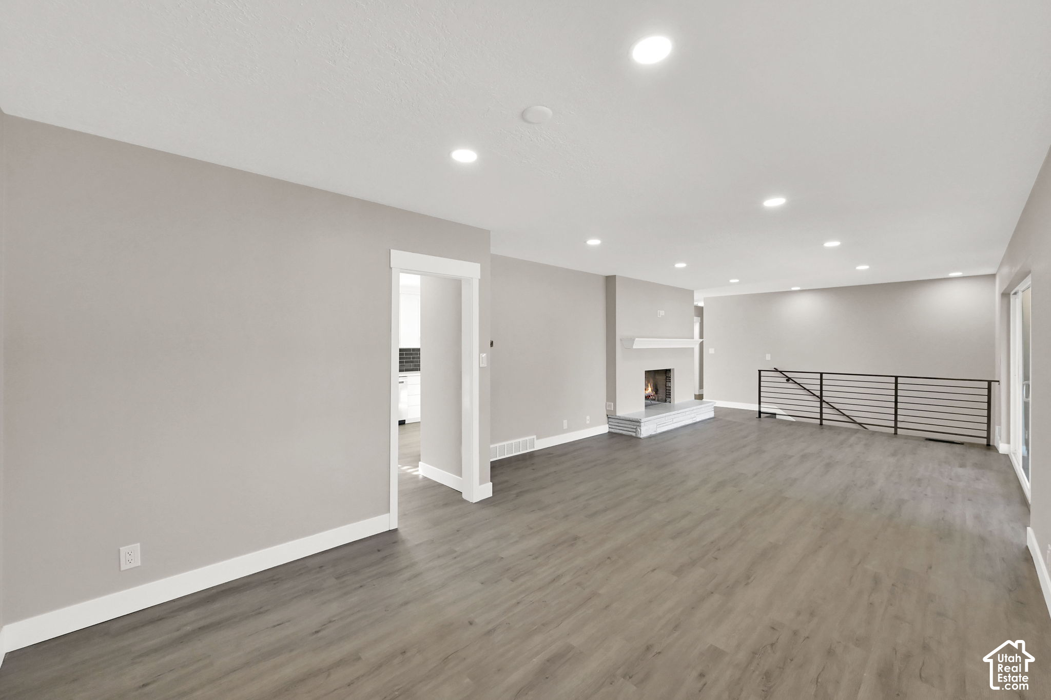 Empty living room with gray flooring, a lit fireplace, and a black metal railing.