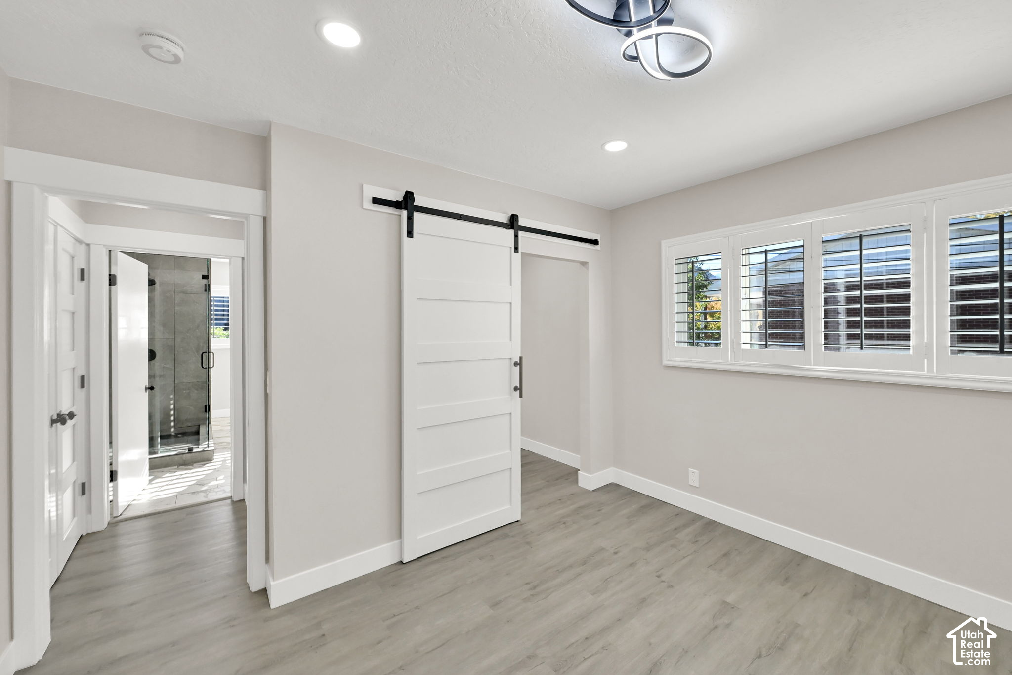 Empty bedroom with gray flooring, a white sliding barn door, and shuttered windows.