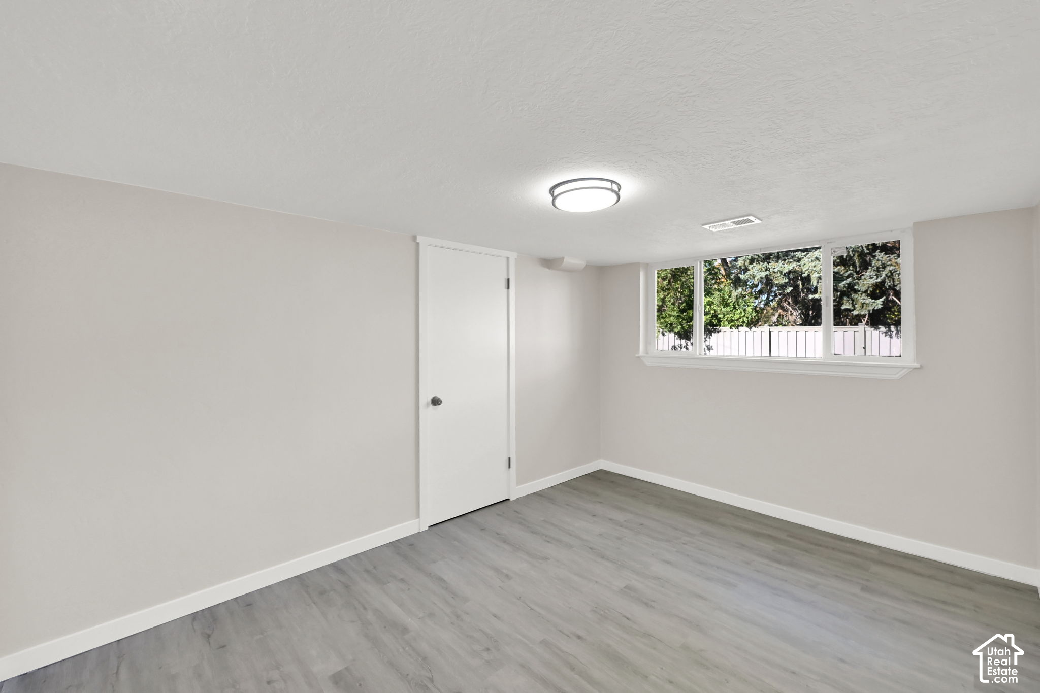 Vacant room with gray flooring, a wide window, and a white door.