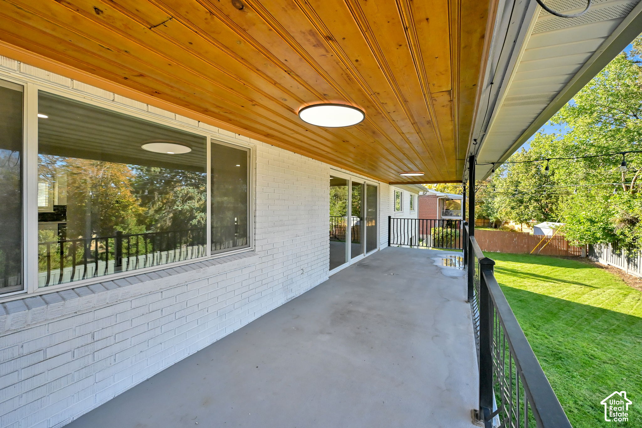 Covered patio with a wood ceiling and black railing overlooking a green backyard.