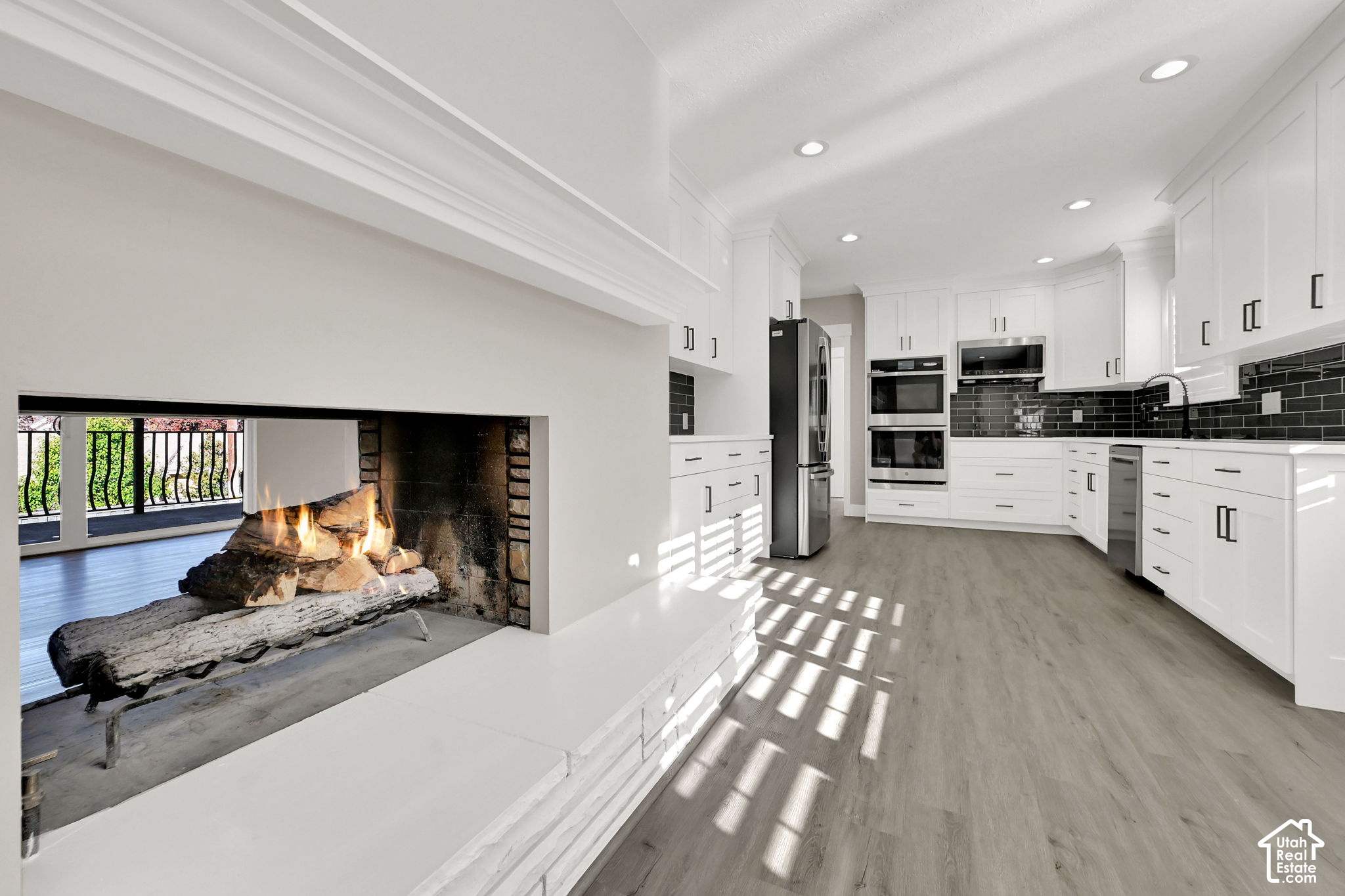 Renovated white kitchen with stainless appliances and a large fireplace in the foreground.