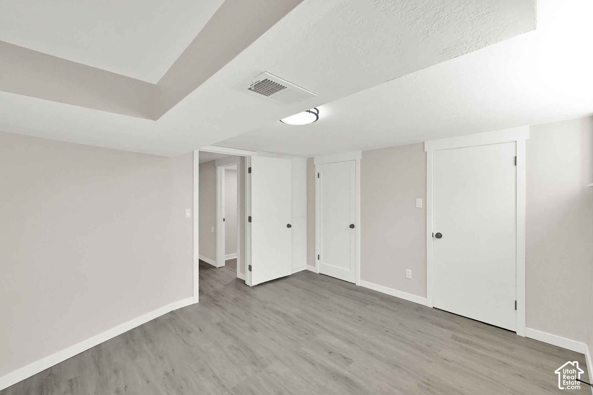 Empty room with gray plank flooring, a tray ceiling, and several white doors.