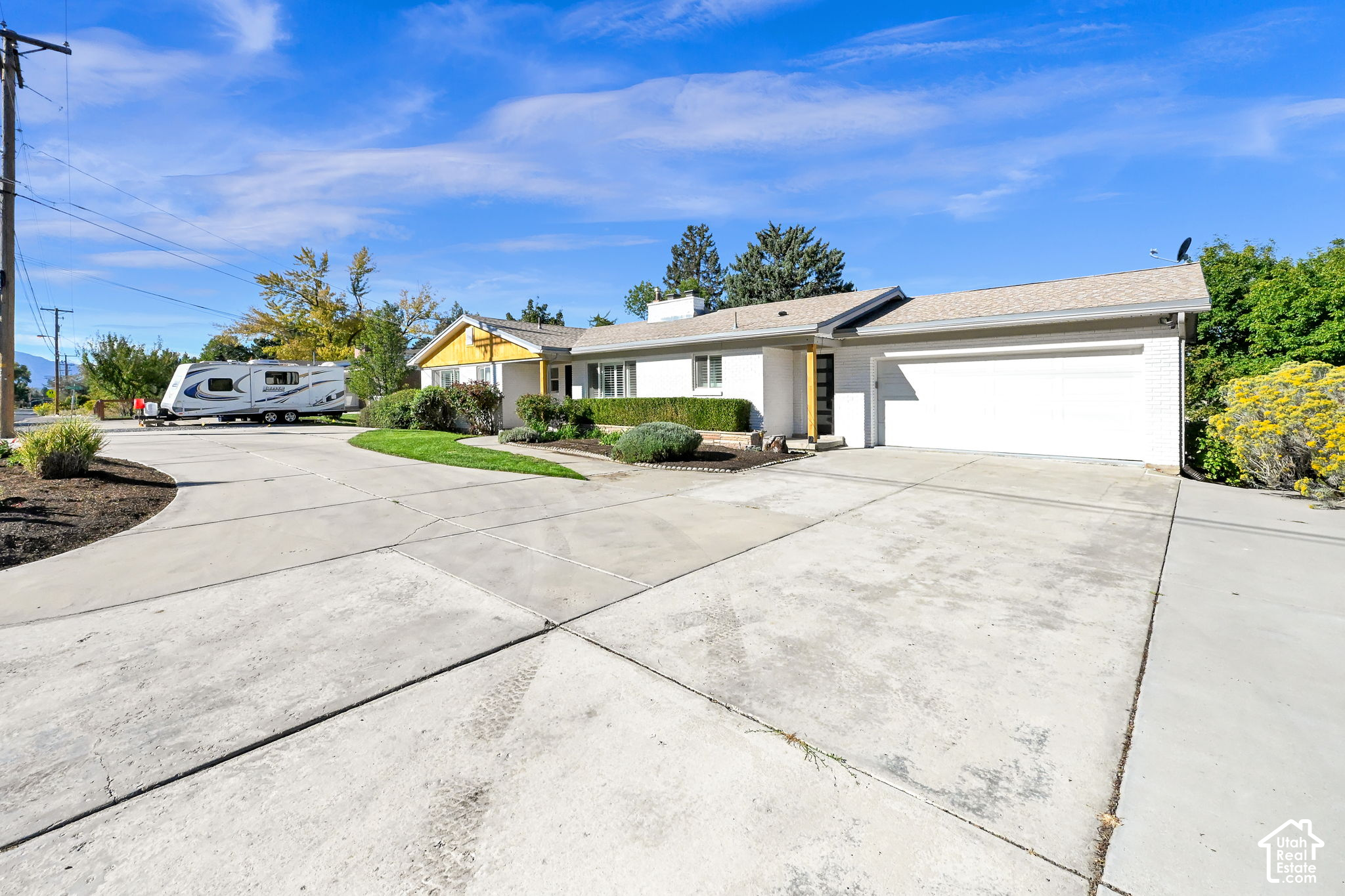 Single-story white brick home with a broad driveway, attached garage, and RV parked beside it.