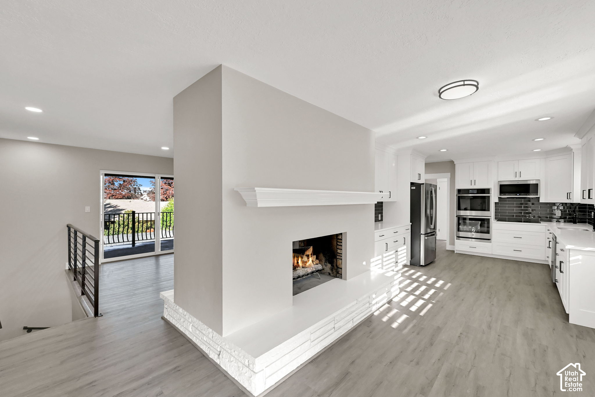 Open kitchen and living area with white cabinets, a central fireplace, and sliding doors to a balcony.