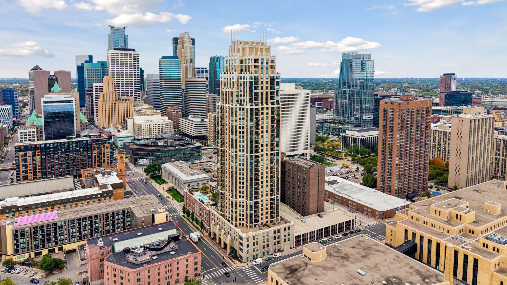 Aerial view of downtown Minneapolis high-rises and rooftops under a partly cloudy sky.