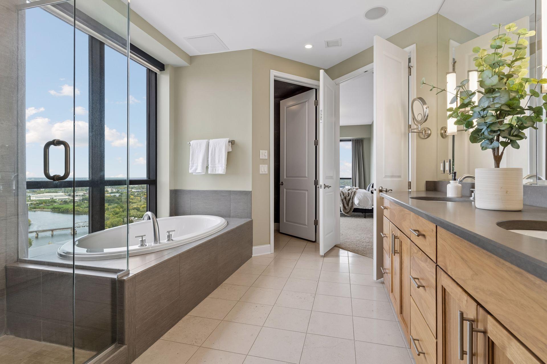 High-rise bathroom with a soaking tub, glass shower, wood vanity, and river view through large windows.