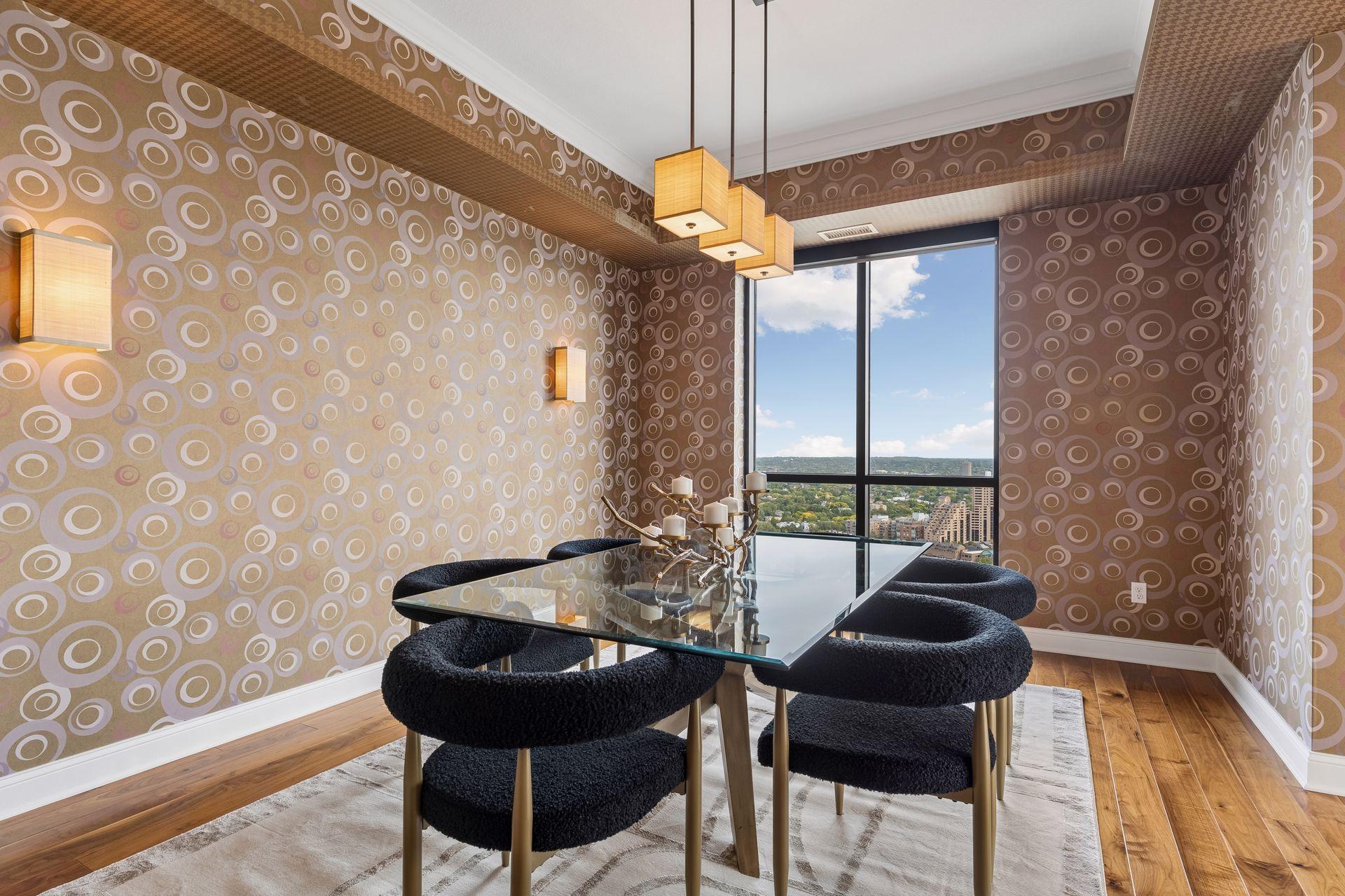 Dining room with a glass table, circular-patterned wallpaper, and a large city-view window.