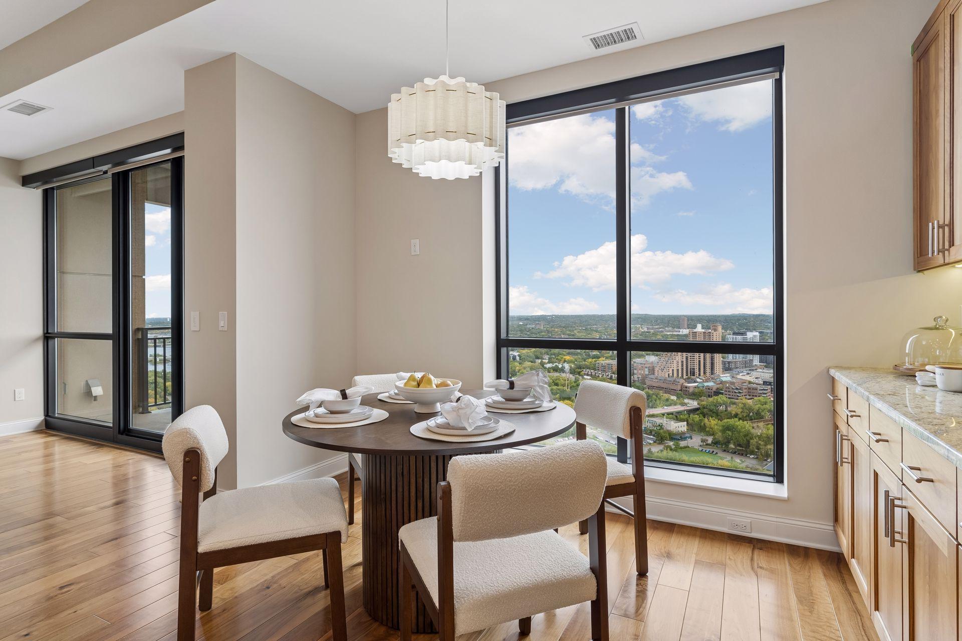 Dining area with a set table beside floor-to-ceiling windows overlooking the city.