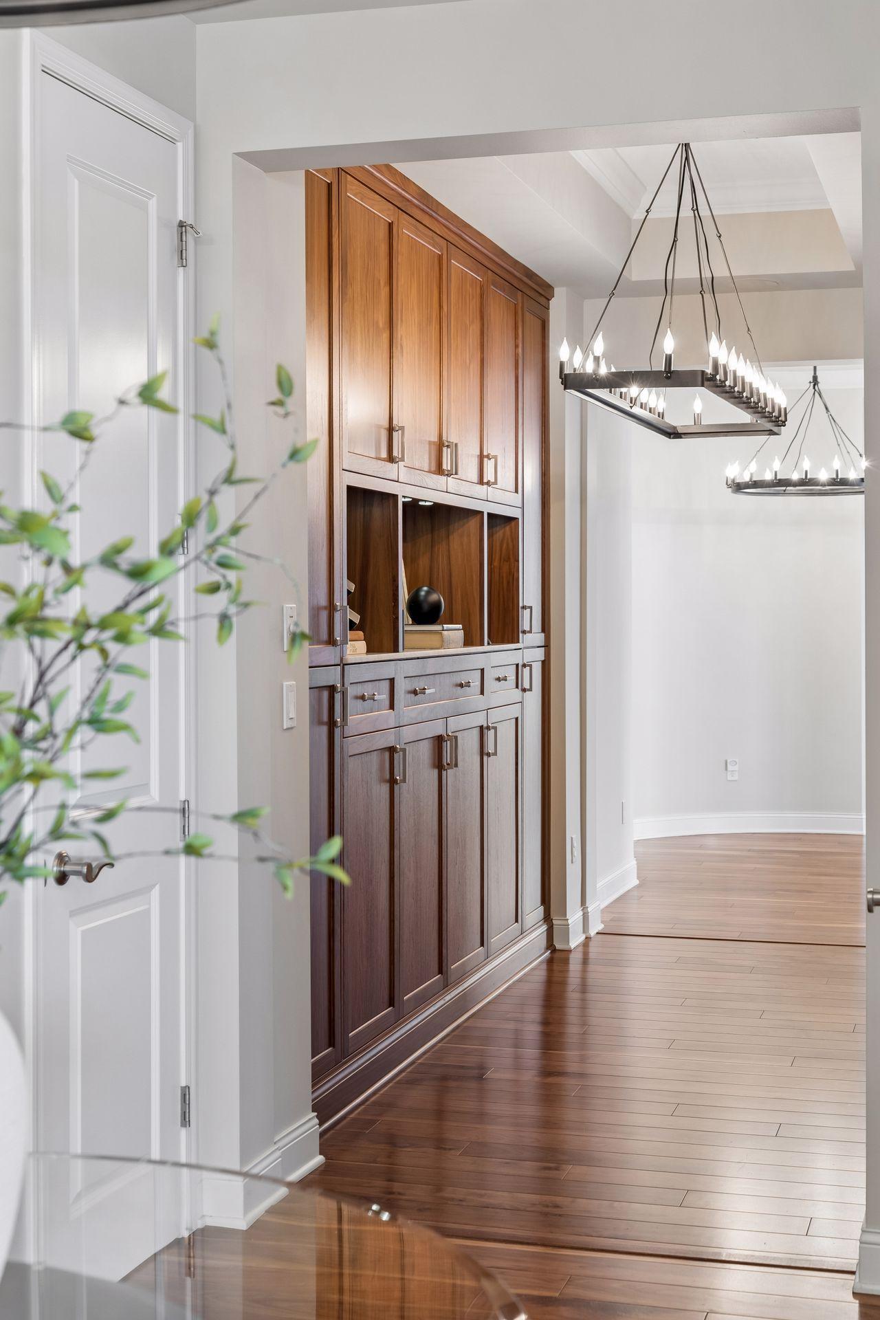 Condo interior with a dark wood built-in cabinet, hardwood floors, and linear chandeliers.