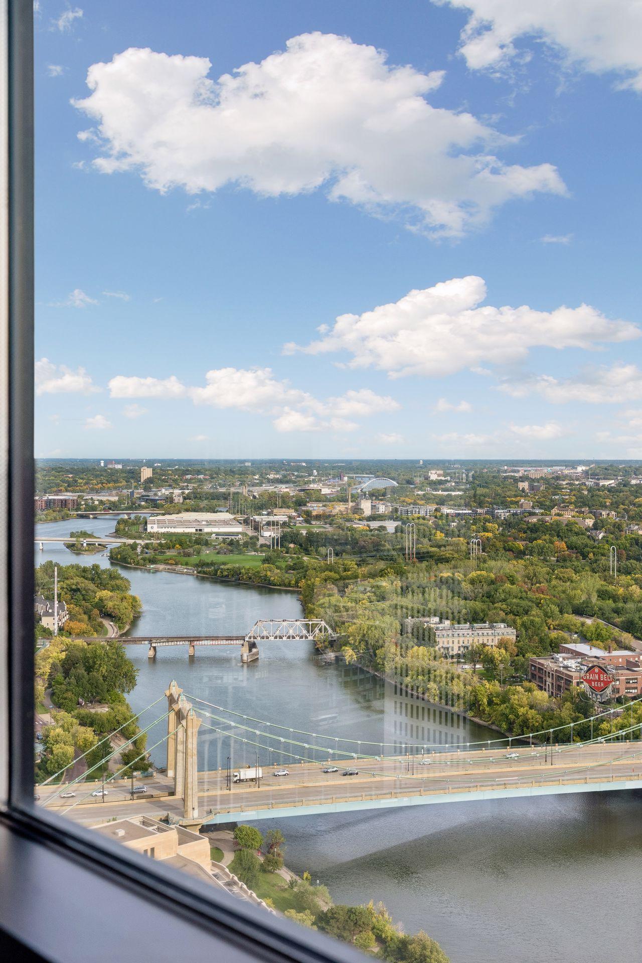Mississippi River and bridges viewed from a high-rise window, with Minneapolis buildings and tree-lined banks.