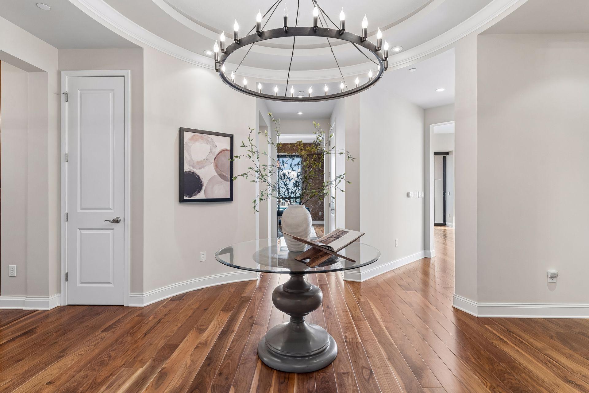 Condominium dining area with a glass table beneath a circular chandelier and polished hardwood floors.