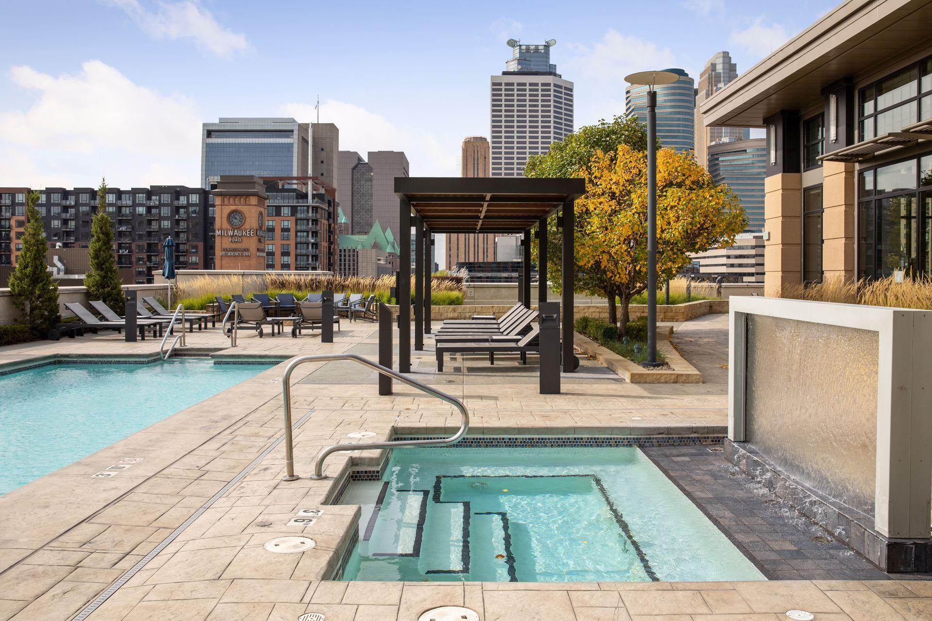 Rooftop pool and spa terrace with pergola, lounge chairs, and downtown Minneapolis skyline.