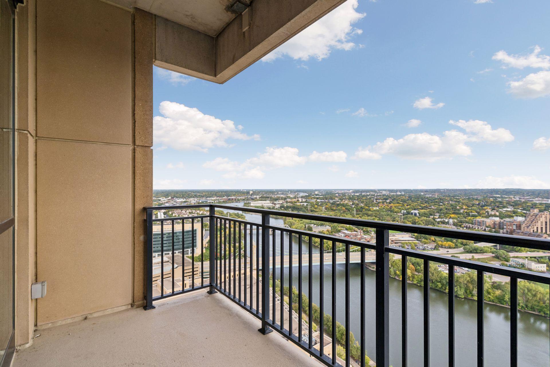 High-rise balcony overlooking a river and tree-lined cityscape.