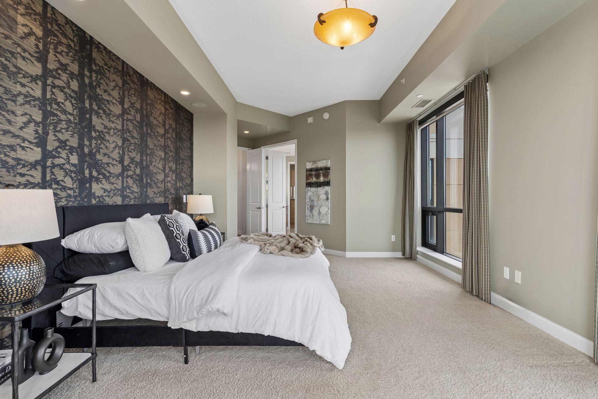 Staged bedroom with a large bed, dark patterned accent wall, and tall curtained windows.