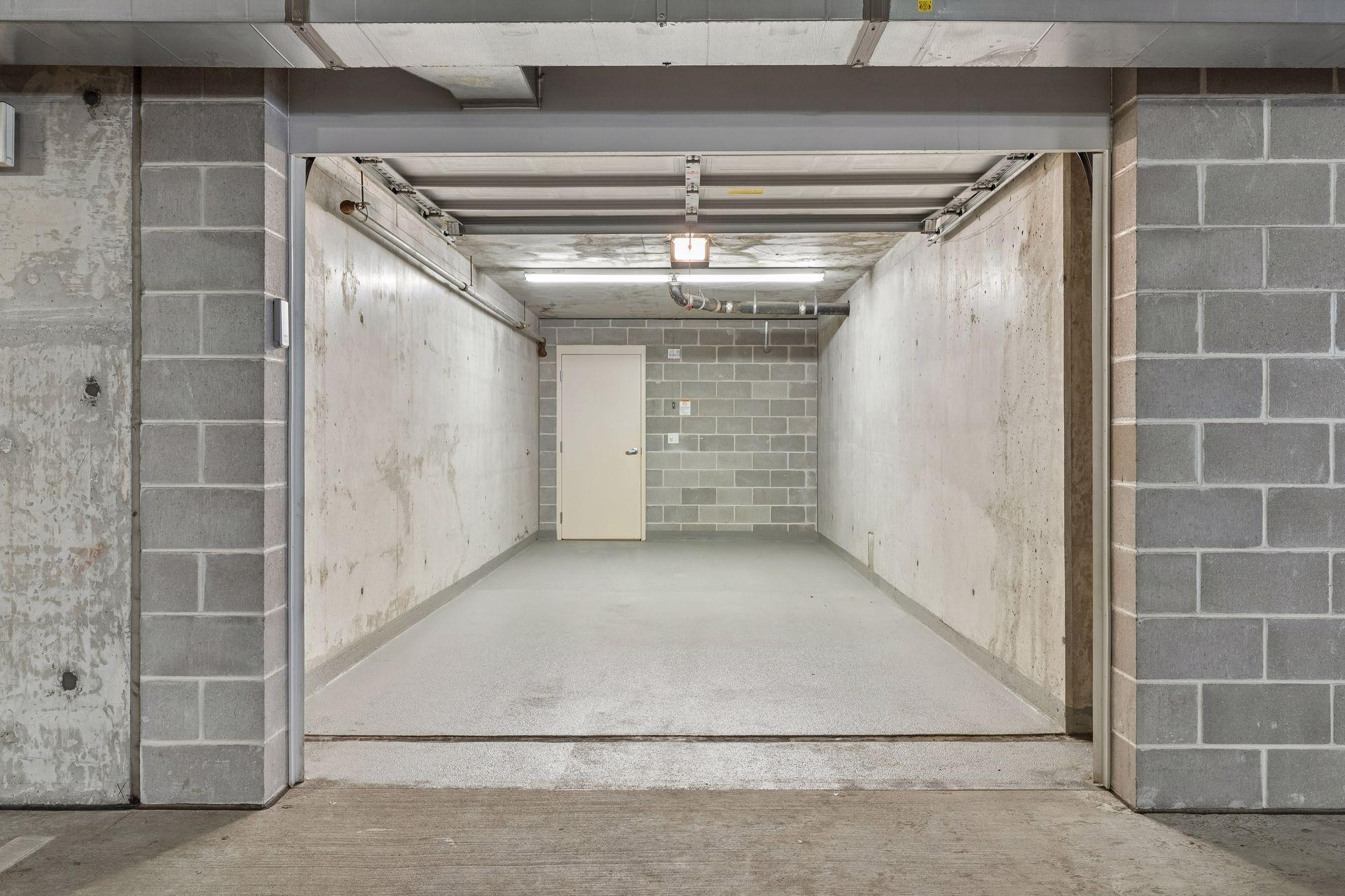 Empty concrete garage stall with an open overhead door and a white door at the rear.