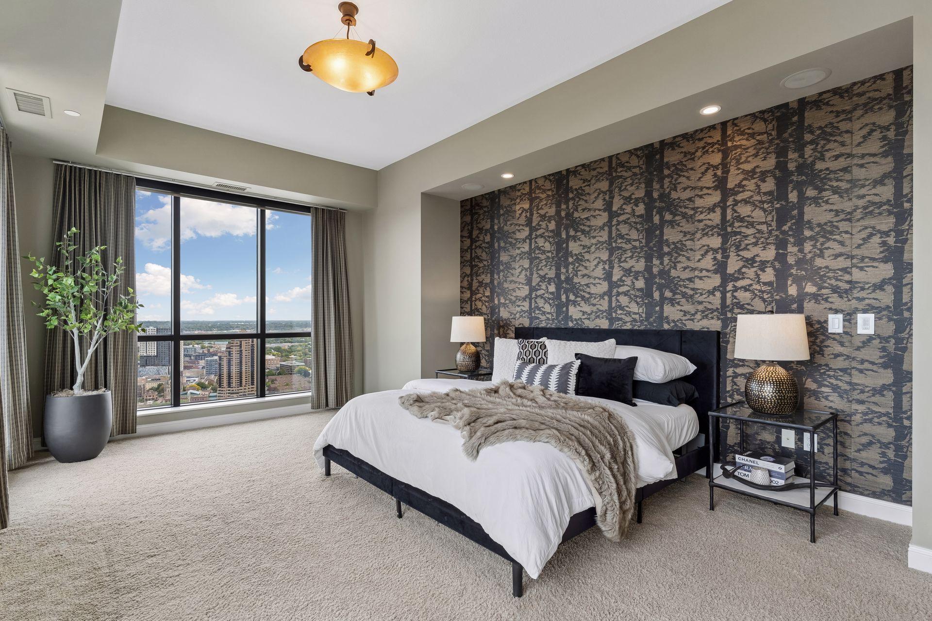 Furnished bedroom with a patterned accent wall and floor-to-ceiling windows overlooking the city.
