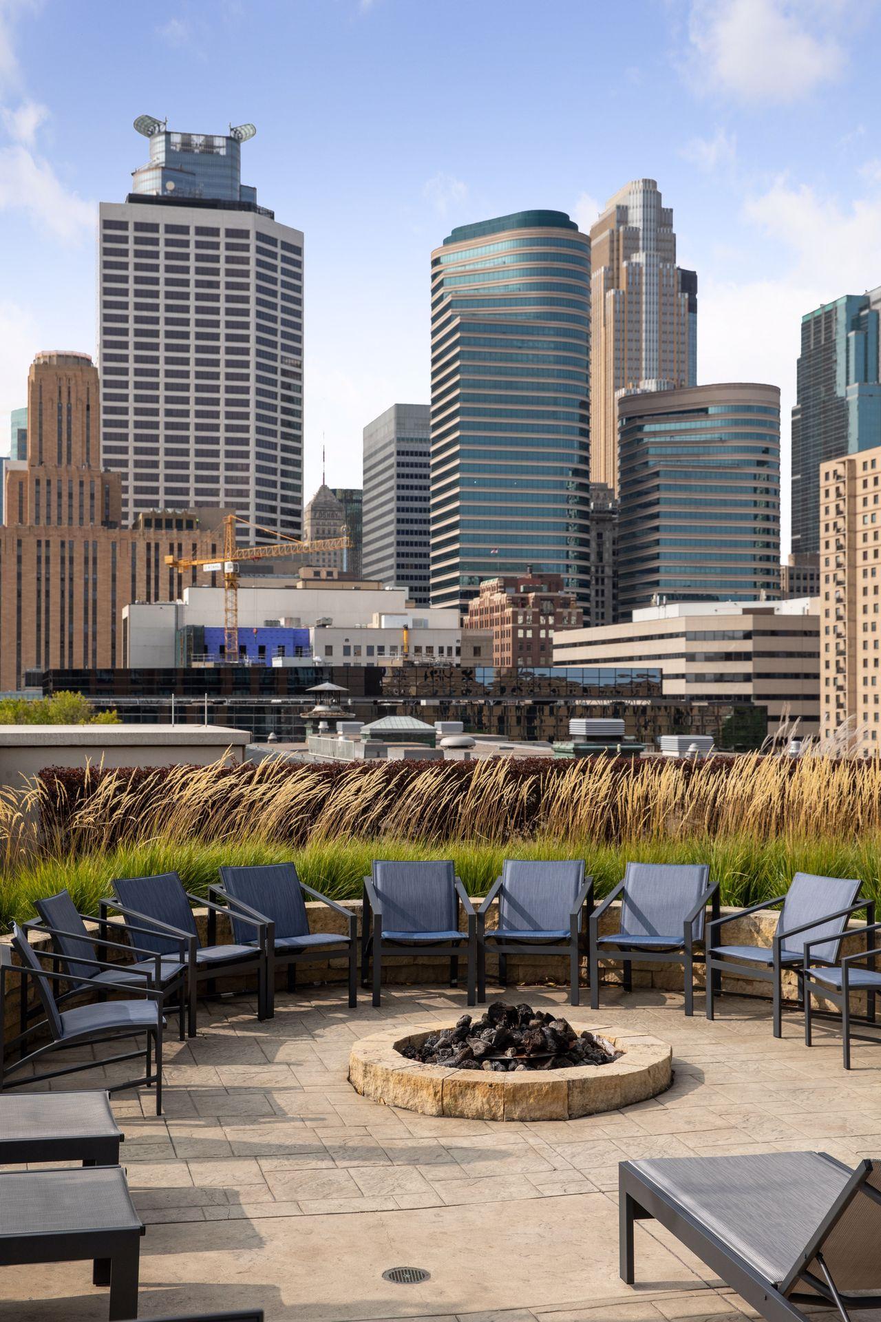 Rooftop terrace with lounge chairs and a fire pit overlooking the Minneapolis skyline.