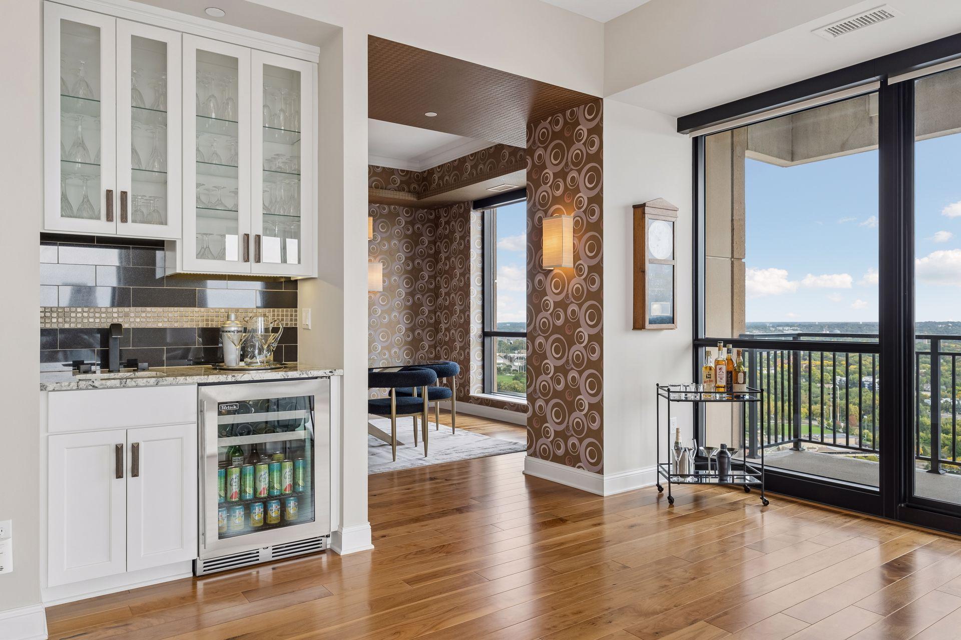 Condo living area with a built-in wet bar and floor-to-ceiling windows overlooking leafy greenery.
