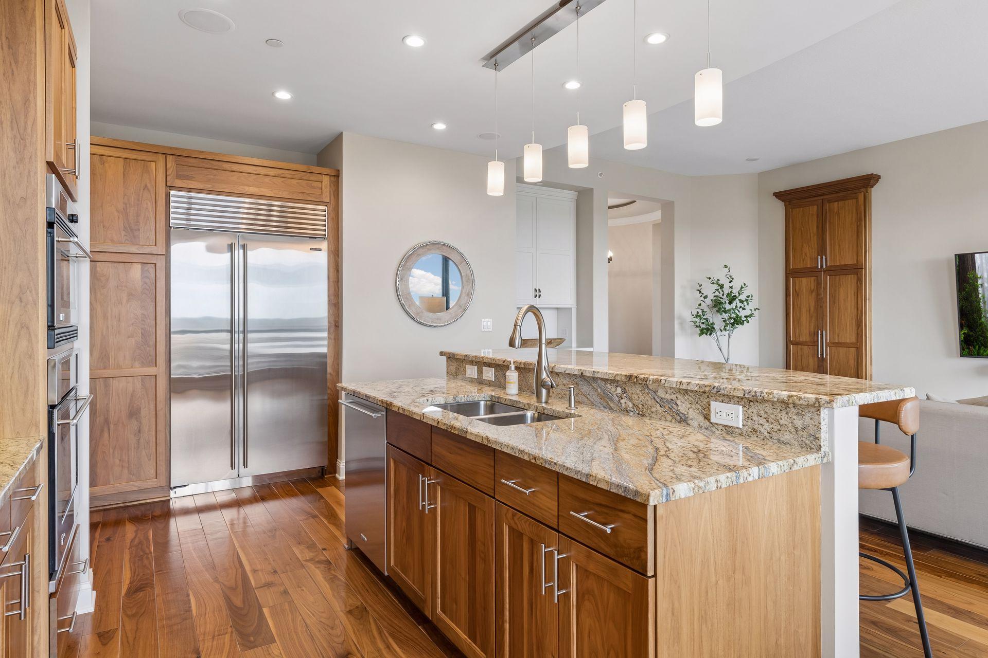 Condo kitchen with a granite island, wood cabinetry, stainless steel appliances, and pendant lights.