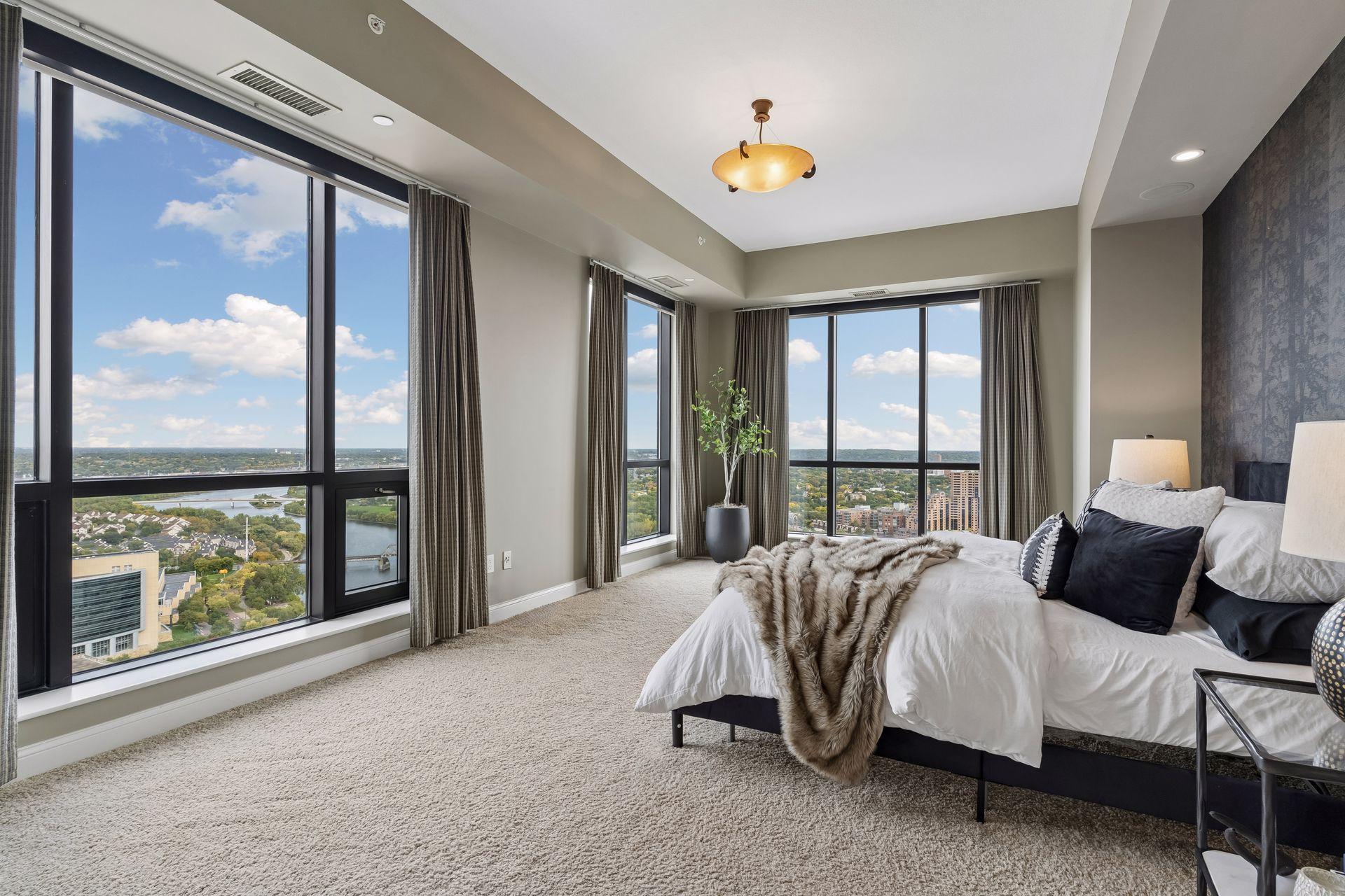 High-rise bedroom with floor-to-ceiling windows overlooking a river and city skyline.
